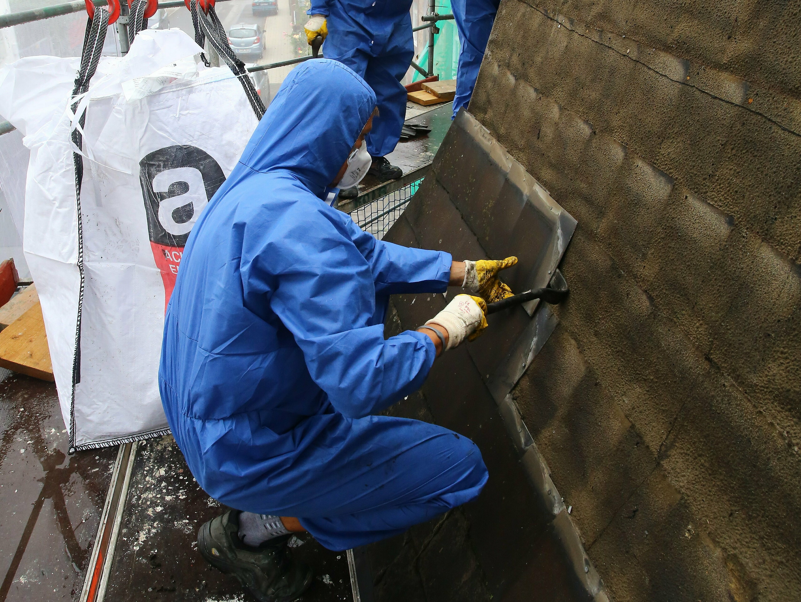 Highly-skilled staff removing and disposing of an old roof covering containing asbestos. They are wearing face masks to stop them breathing in the asbestos.