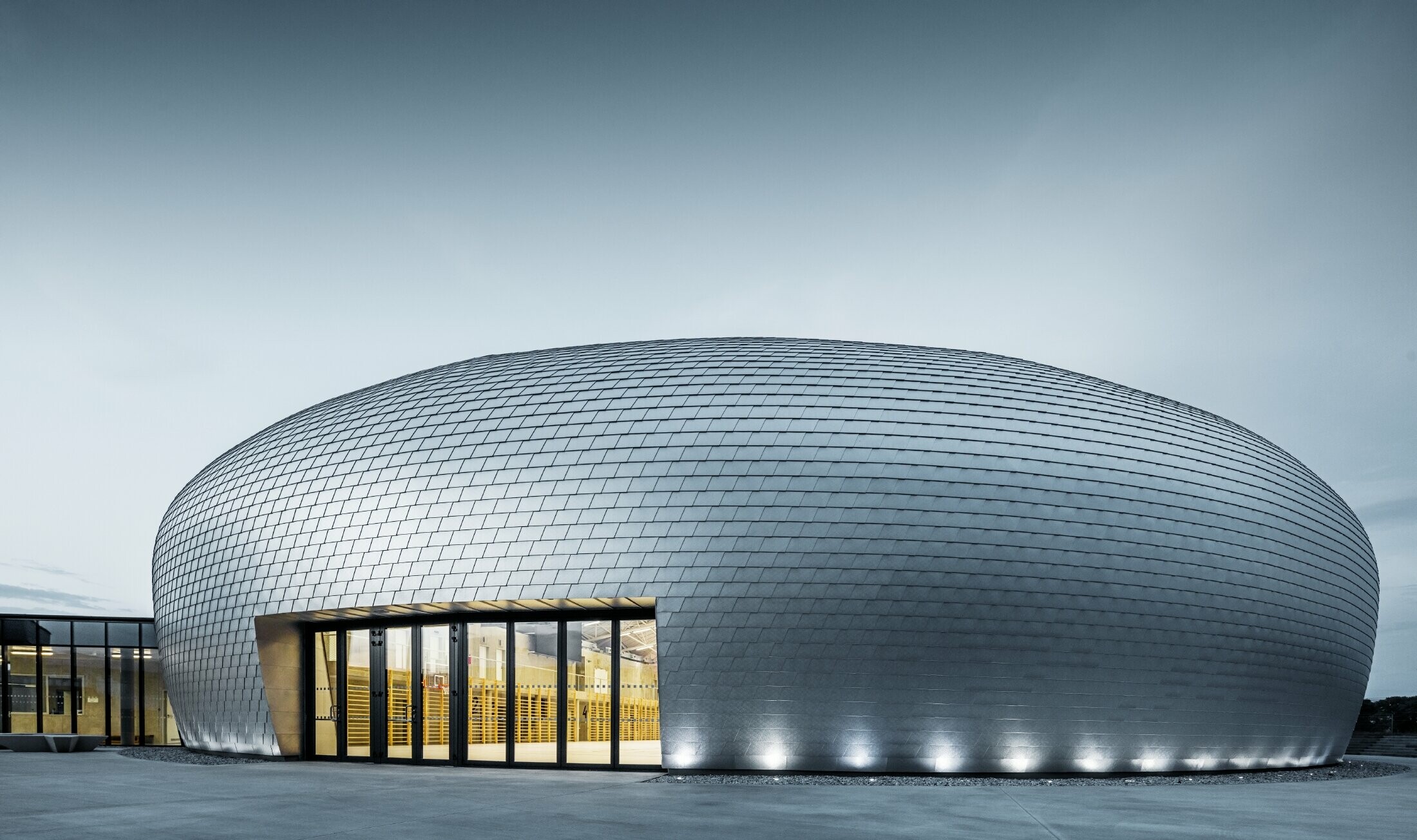 Photo of the sports hall in the Czech Republic in the shape of a UFO clad in the PREFA façade shingle in plain aluminium.