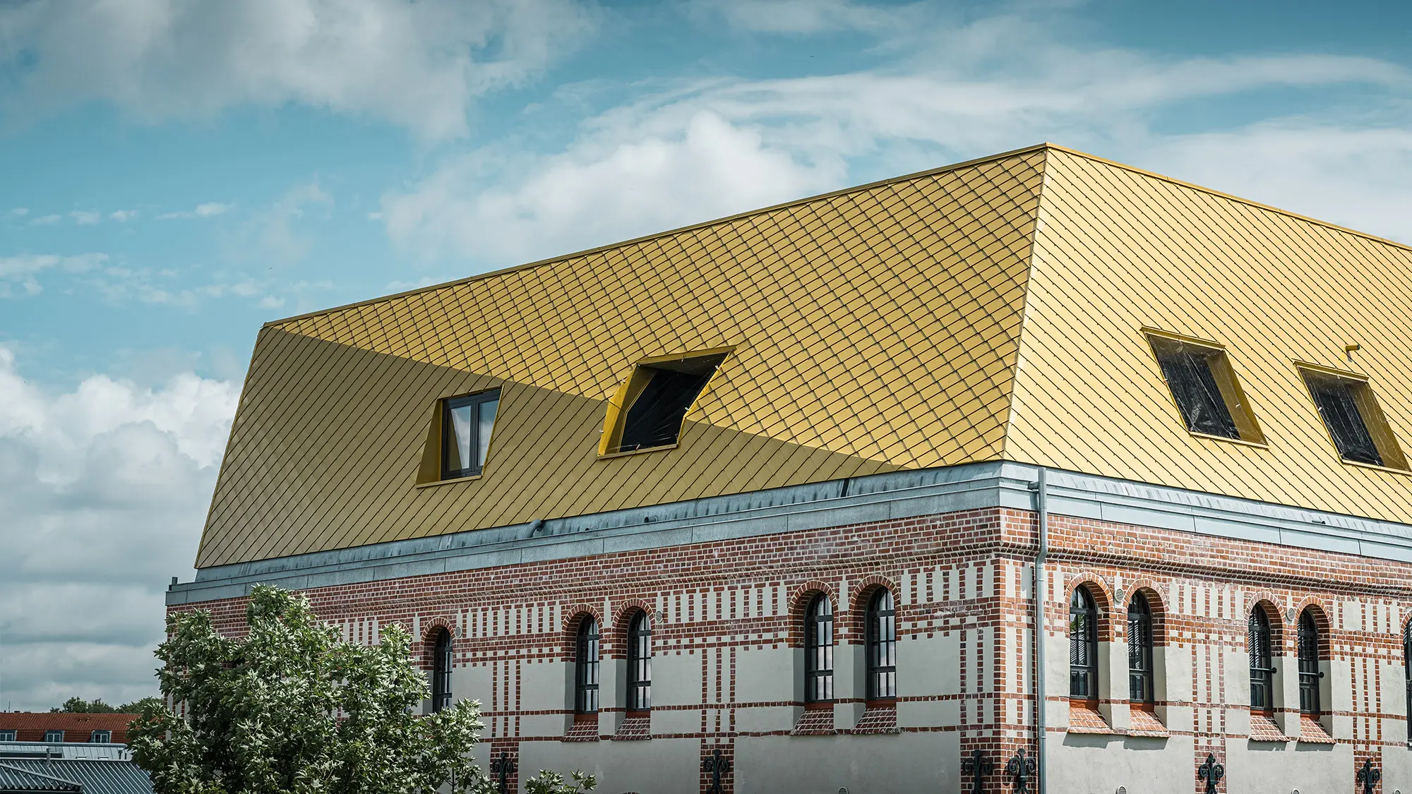 The roof with the Maya gold aluminium rhomboid tiles and a fold from up close, part of the listed façade can be seen.