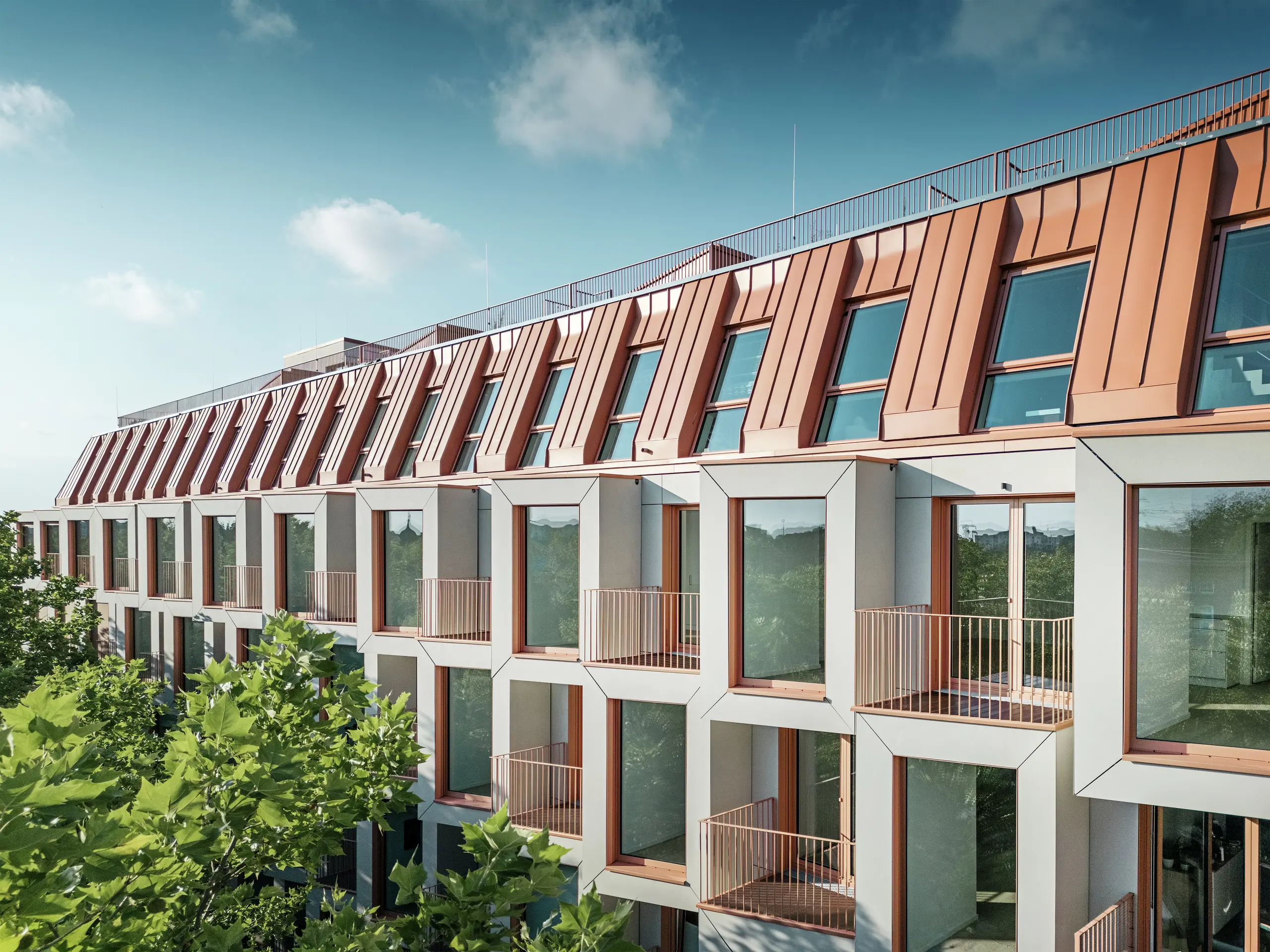Facade view of the Van B residential project in Munich with the striking PREFALZ aluminium roof in the special colour IGP Orange HDP from PREFA. The modern roof covering combines aesthetic elegance with technical precision and offers lasting protection against the elements. The cubic bay windows with generous window areas and filigree balconies create a harmonious interplay of light, space and functionality – ideal for sophisticated living concepts in urban environments.