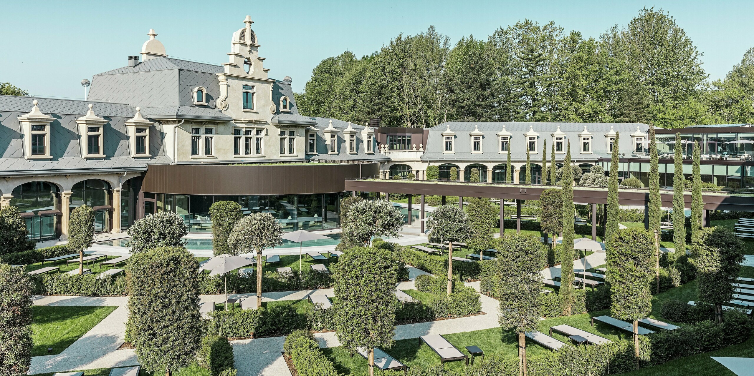 Der sorgfältig restaurierte Thermalpark „De Montel – Terme Milano“ verfügt über eine moderne Gartenlandschaft mit geradlinigen Wegen, Liegezonen und mediterraner Bepflanzung ein. Die stilvolle Dacheindeckung mit der PREFA Dachraute 44 × 44 in P.10 Hellgrau betont die historische Architektur, während moderne Glaselemente und ein begrüntes Vordach die Verbindung zur zeitgenössischen Nutzung herstellen.