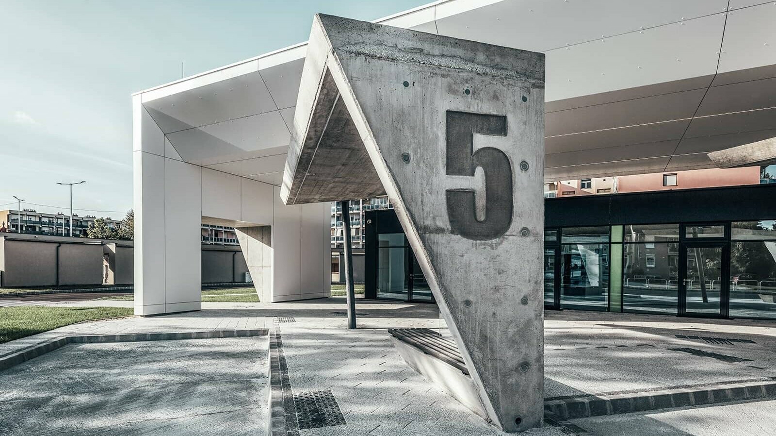 The picture shows a concrete pillar with the number 5. A section of the railway station in Lenti can be seen in the background. You can also see the white façade, which is covered in PREFABOND aluminium composite panels.