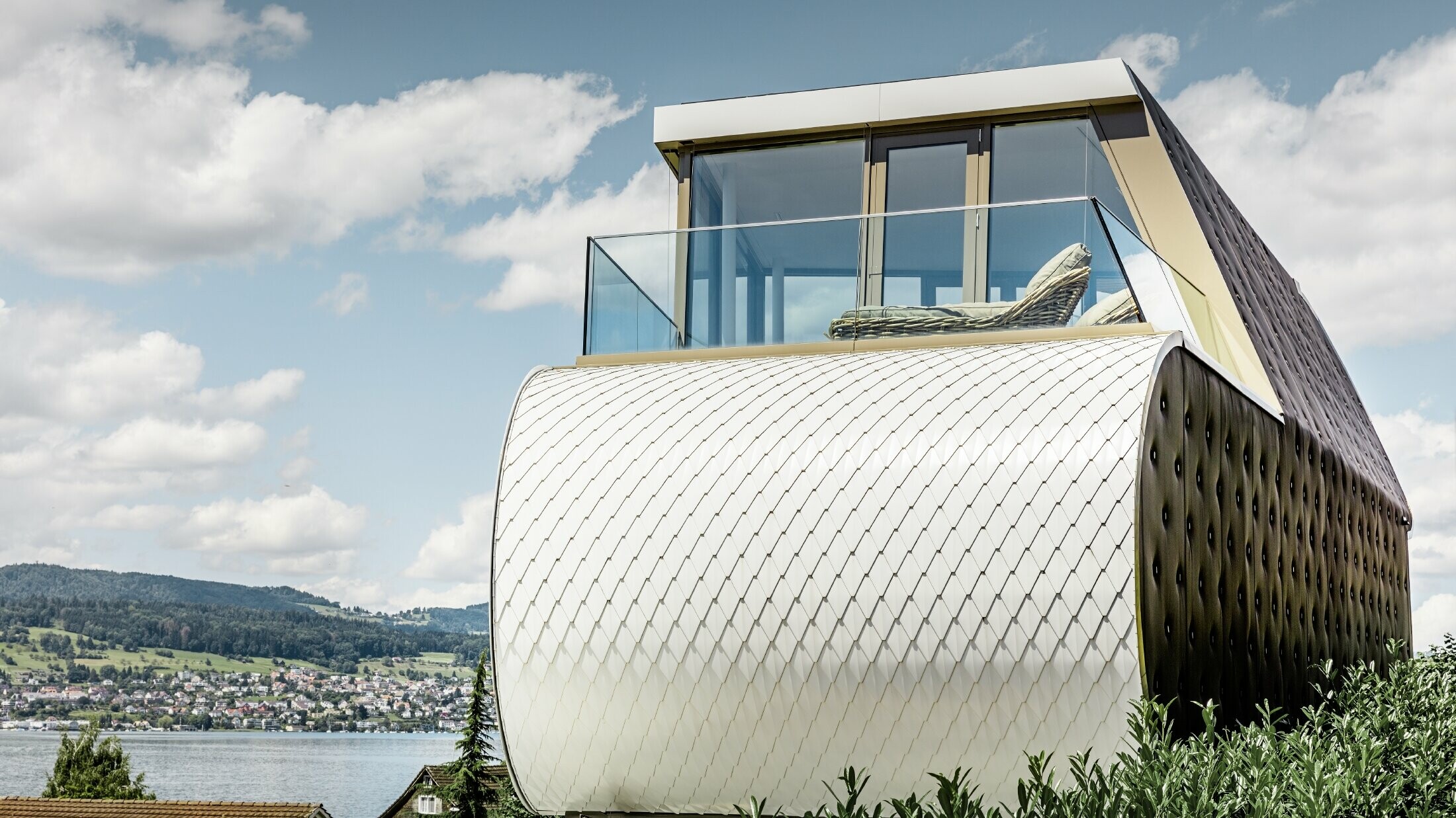 Side view of the excellent Flexhouse, designed by the architect Camenzind; you can see one of the curved exterior walls, which is clad with PREFA’s scale-like aluminium façade in pure white.