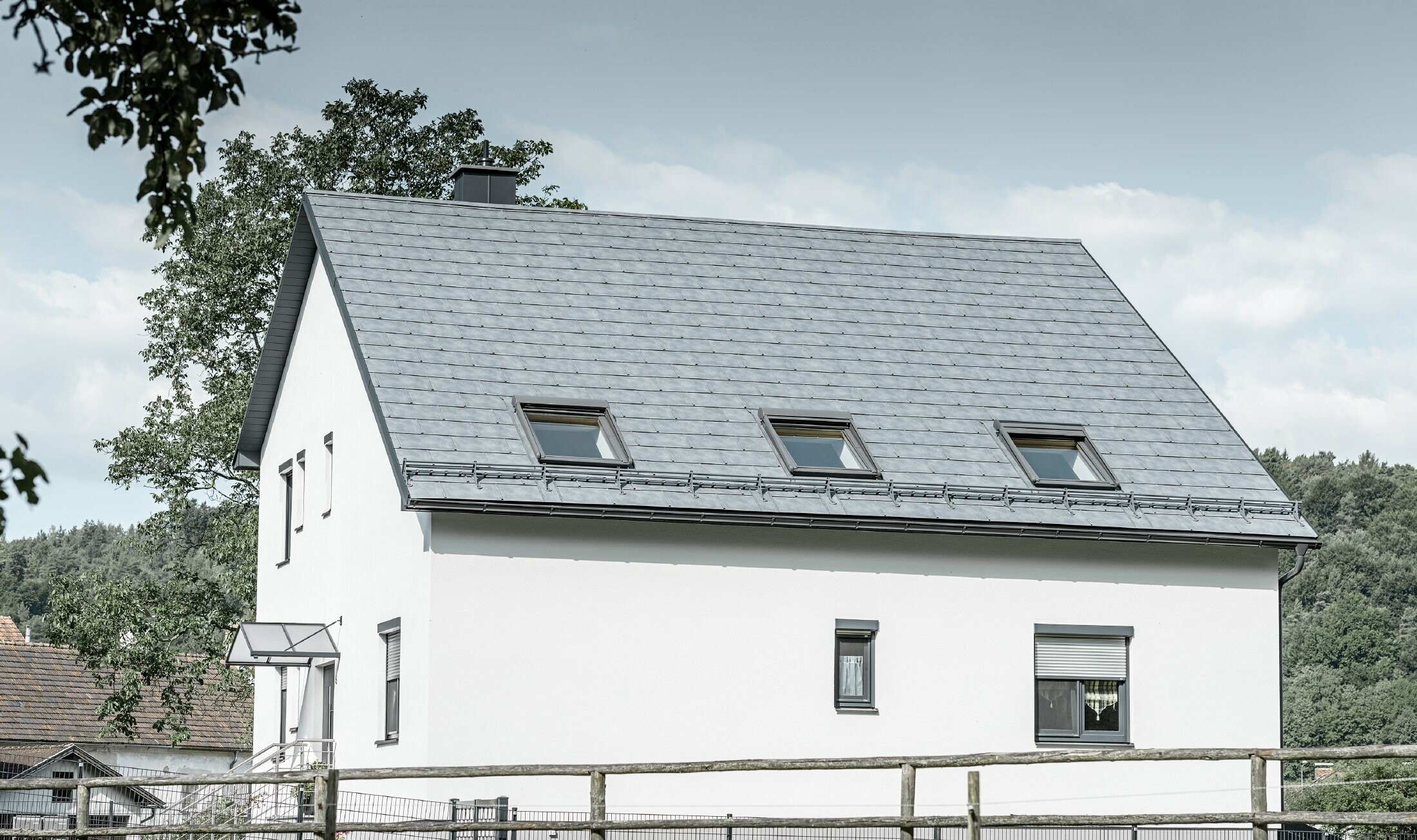 The gabled roof of the classic detached house was covered with the new PREFA R.16 roof tile in stone grey. Three roof windows were inserted in the roof area and snow guards were installed. The façade is kept simple in white.