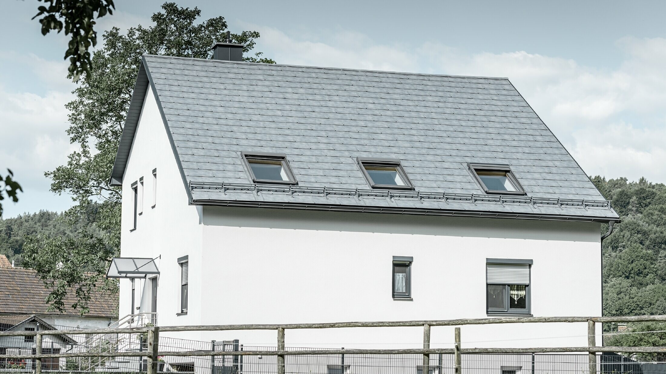 The gabled roof of the classic detached house was covered with the new PREFA R.16 roof tile in stone grey. Three roof windows were inserted in the roof area and snow guards were installed. The façade is kept simple in white.