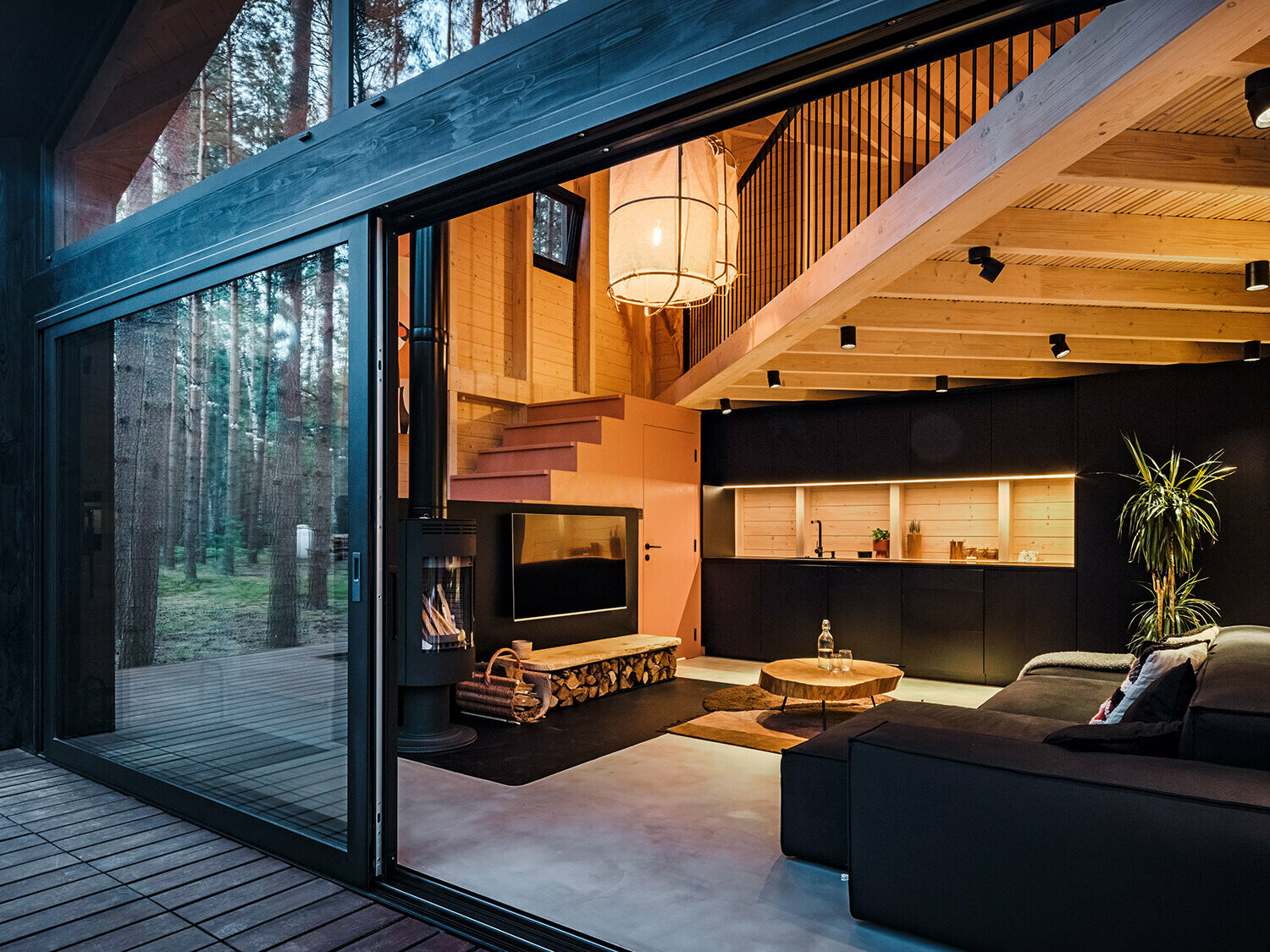 A closer look into the lighted interior of the structure with its wooden paneling, cosy living and dining area, and the staircase ascending to the bedroom. 