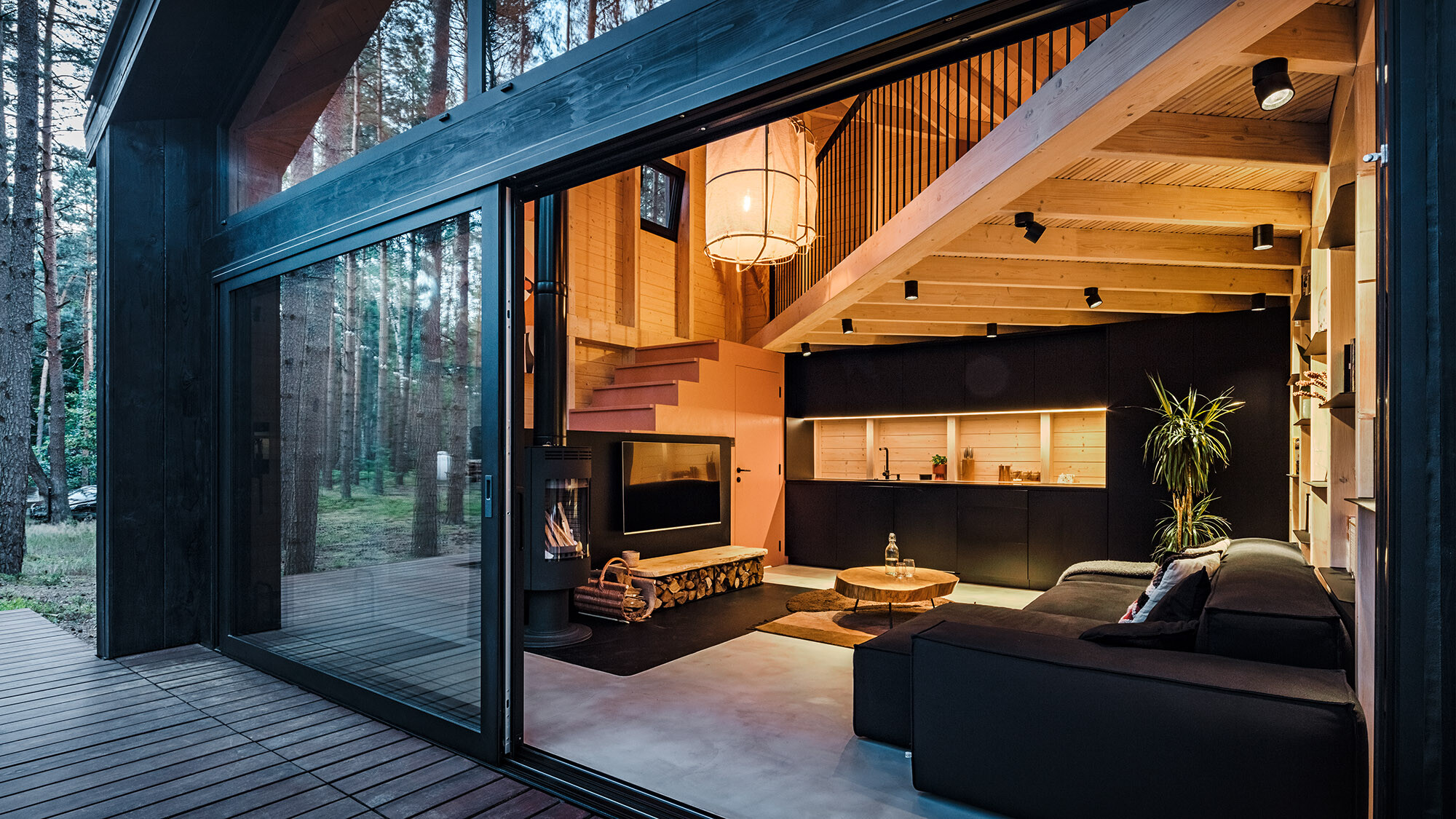 A closer look into the lighted interior of the structure with its wooden paneling, cosy living and dining area, and the staircase ascending to the bedroom. 