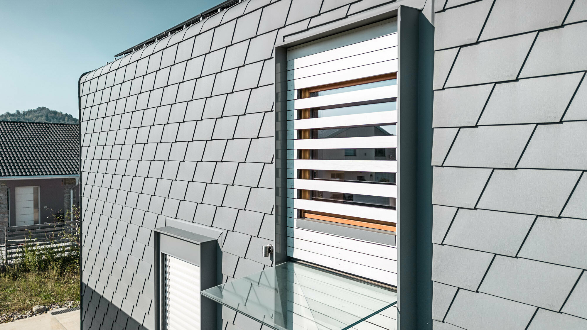 Detailed view of the façade with the accurately laid light-grey shingles.