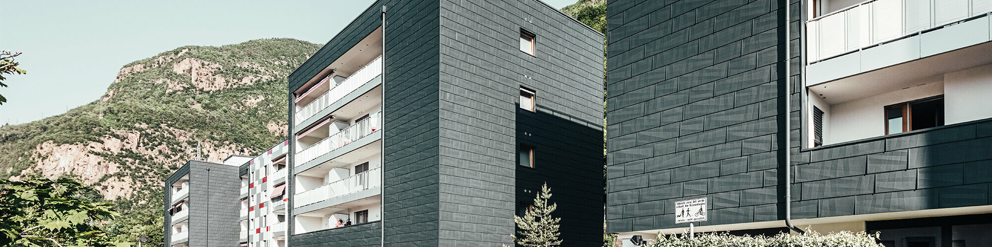 Diagonal view from the front of the renovated residential building in Bolzano. Balconies with white railings and house façade realised with the product facade panel FX.12.