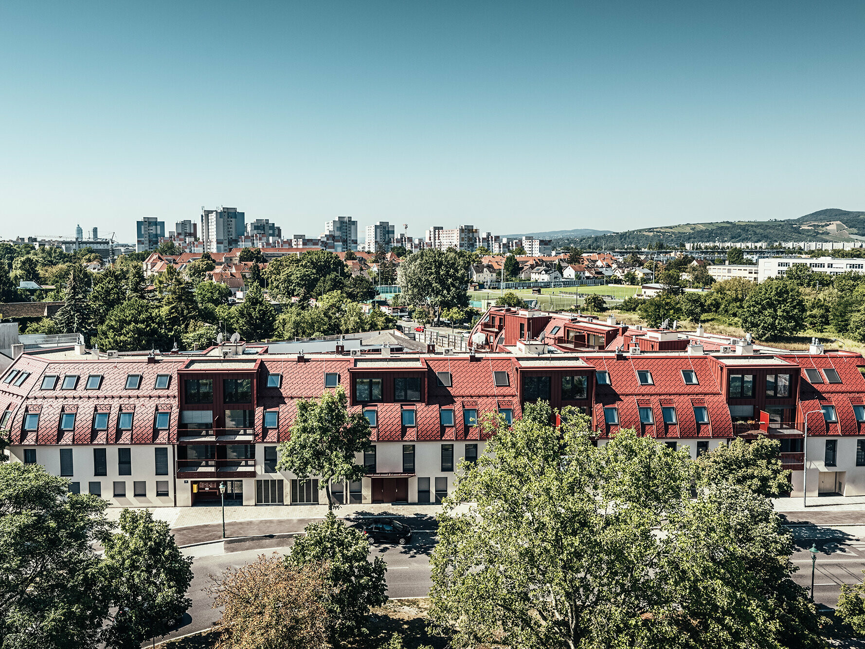 Bird's eye view of the entire residential building and its surrounding area, far behind it the urban fabric.