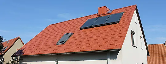 Detached house with gable roof covered with PREFA roof tiles in brick red. Roof includes solar panels and skylight
