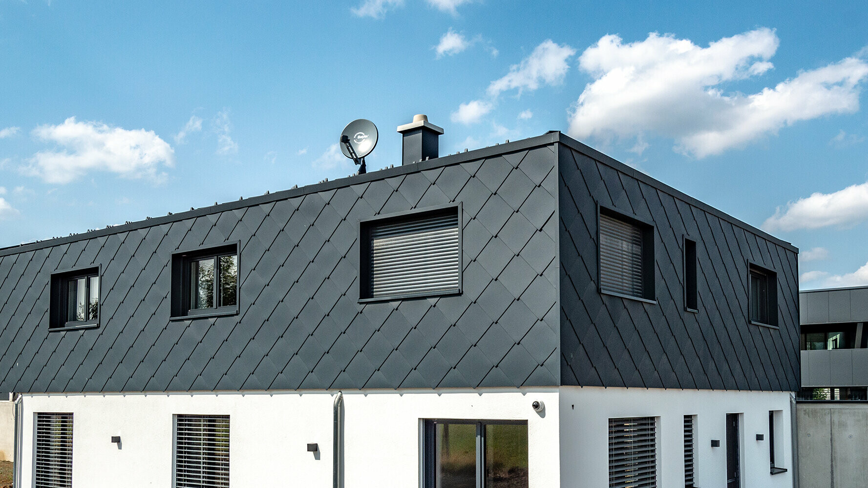 Modern new building with flat roof, the upper floor is clad with the PREFA  44 × 44 rhomboid façade tile in P.10 anthracite, the ground floor is plastered white.