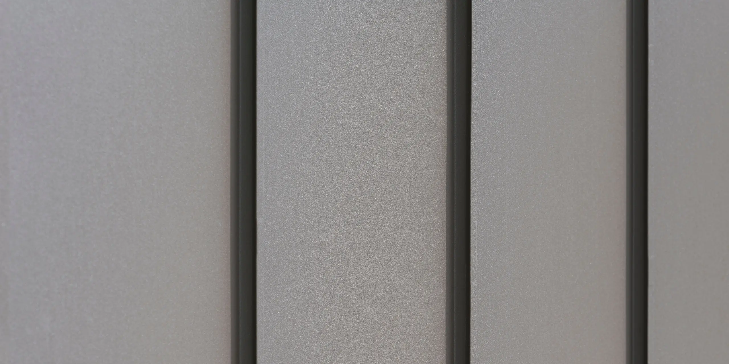 Nahaufnahme einer modernen Fassadenverkleidung aus Aluminium mit vertikalen Scharen, die für ein ästhetisch strukturiertes Muster sorgen. Das Aluminium kommt von der PREFA Aluminiumprodukte GmbH.