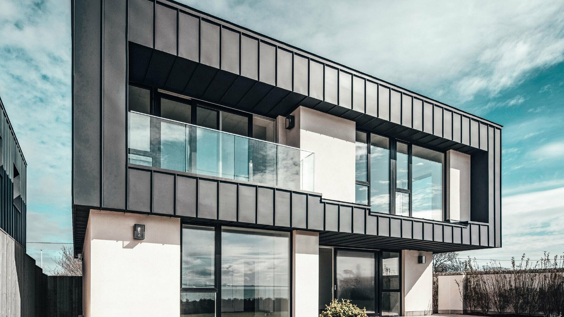 Modern terraced house with flat roof, the facade on the upper floor was designed with an angled standing seam facade made of PREFALZ in anthracite.