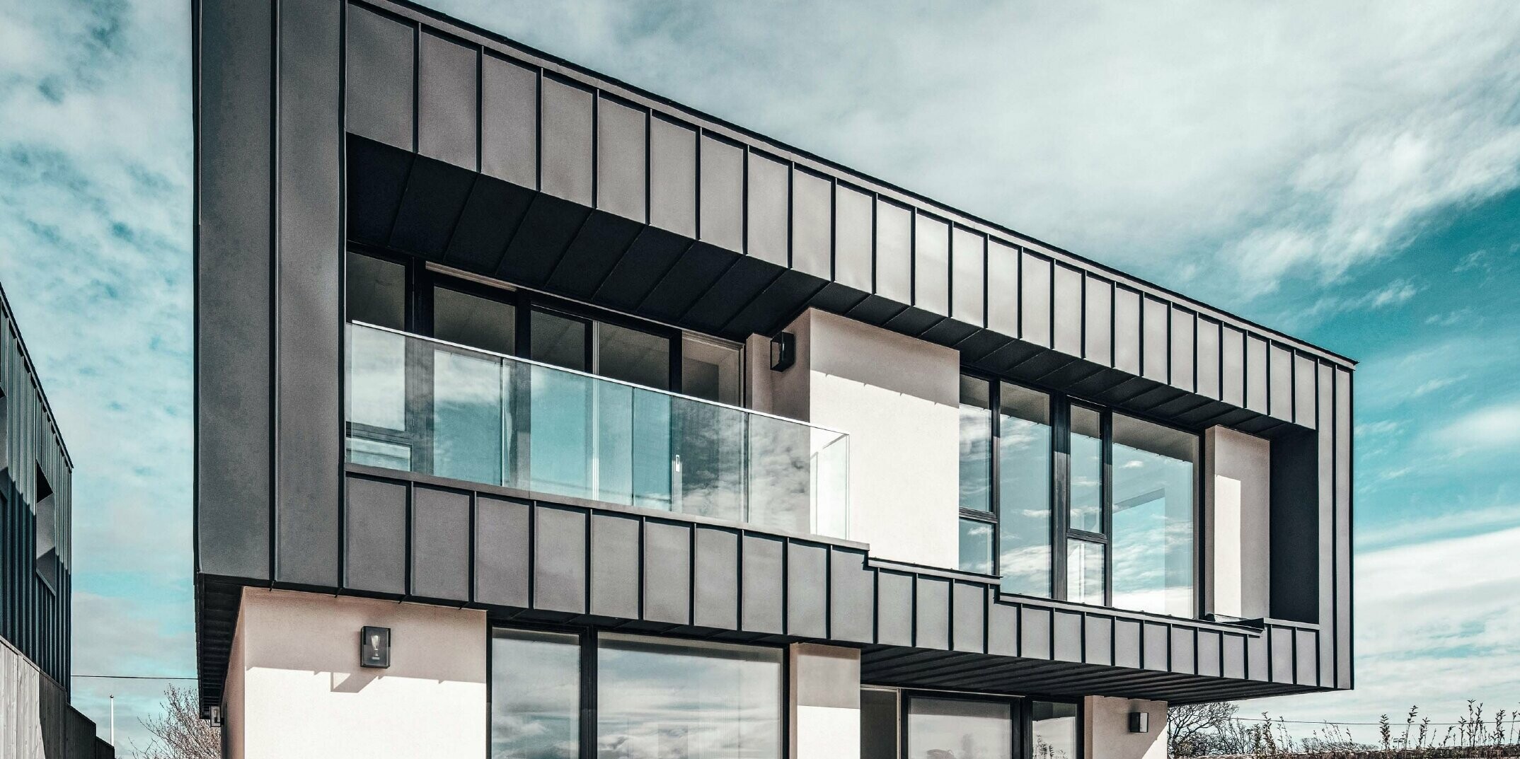 Modern terraced house with flat roof, the facade on the upper floor was designed with an angled standing seam facade made of PREFALZ in anthracite.