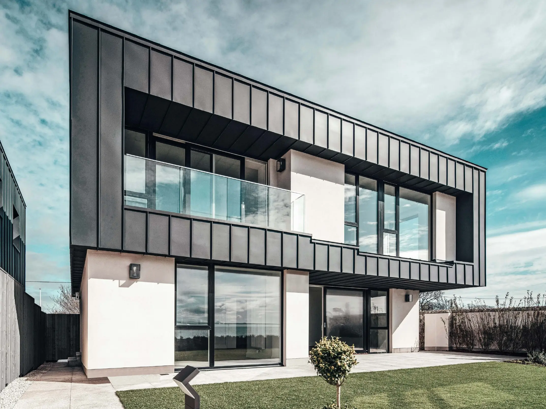 Modern terraced house with flat roof, the facade on the upper floor was designed with an angled standing seam facade made of PREFALZ in anthracite.