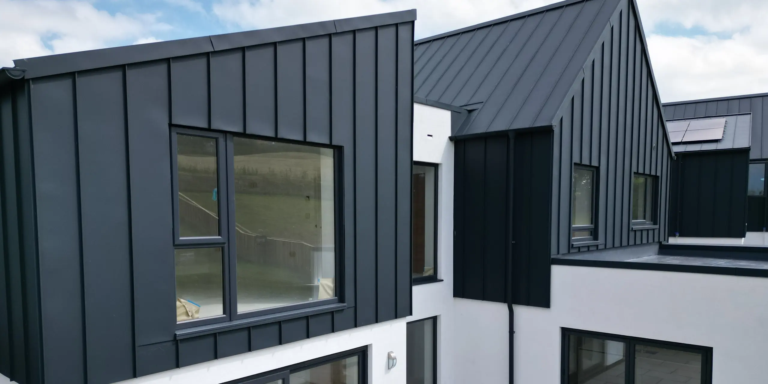 Detailed view of a single-family-house with garden and terrace, covered with PREFALZ standing seam in P.10 anthracite. The aluminium standing seam roof combines modern design with durability and underlines the sustainable approach to construction. The large window areas ensure plenty of light in the interior.