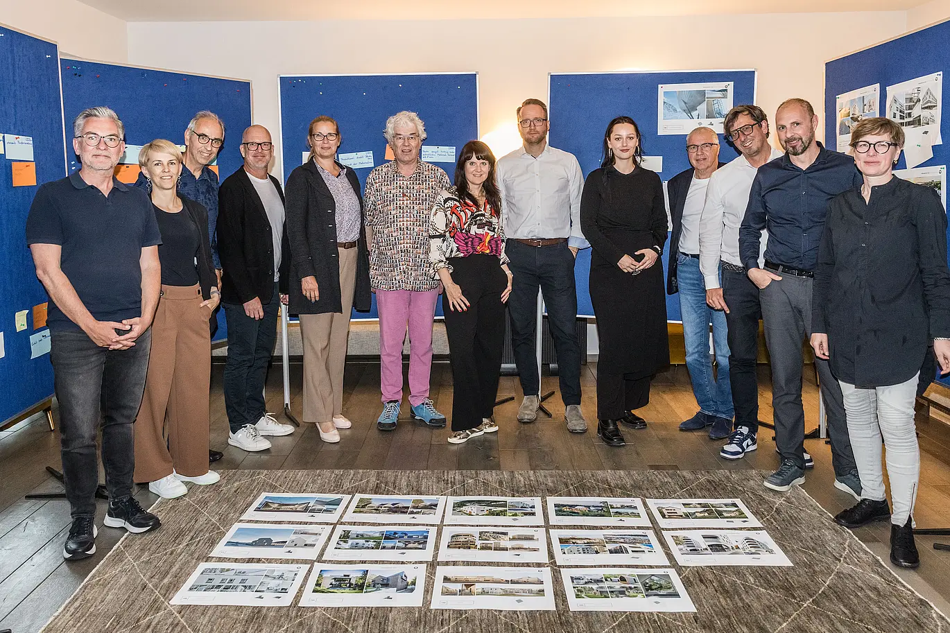 Group photo of the PREFARENZEN 2026 jury after the successful selection process in a winegrower's residence in Seewinkel, Burgenland: The interdisciplinary group of experts consisting of Dirk Lorenz (Leinert Lorenz Architekten), Veronika Roll (Marketing, PREFA Austria), Wolfgang Croce (Croce & Wir, Graz), Jürgen Jungmair (Head of International Marketing, PREFA), Judit Nemere (Managing Director, PREFA Hungary), Matthias Finkentey (Moderator), Bettina Almeida (Communications Management, PREFA), Christian Wirth (Regional Manager East, PREFA Austria), Selina Wach (Head of Discourse, Architektur Aktuell), Thomas Schlett (B3 Architekten), Sven Disser (Head of Development, Bauwerk), Falk Leinert (Leinert Lorenz Architekten) and Juliane Croce (Croce & Wir, Graz) stands in front of the final architectural projects selected for the PREFARENZEN architecture book and the 2026 calendar. The projects reflect diversity, sustainability and innovative use of PREFA materials.