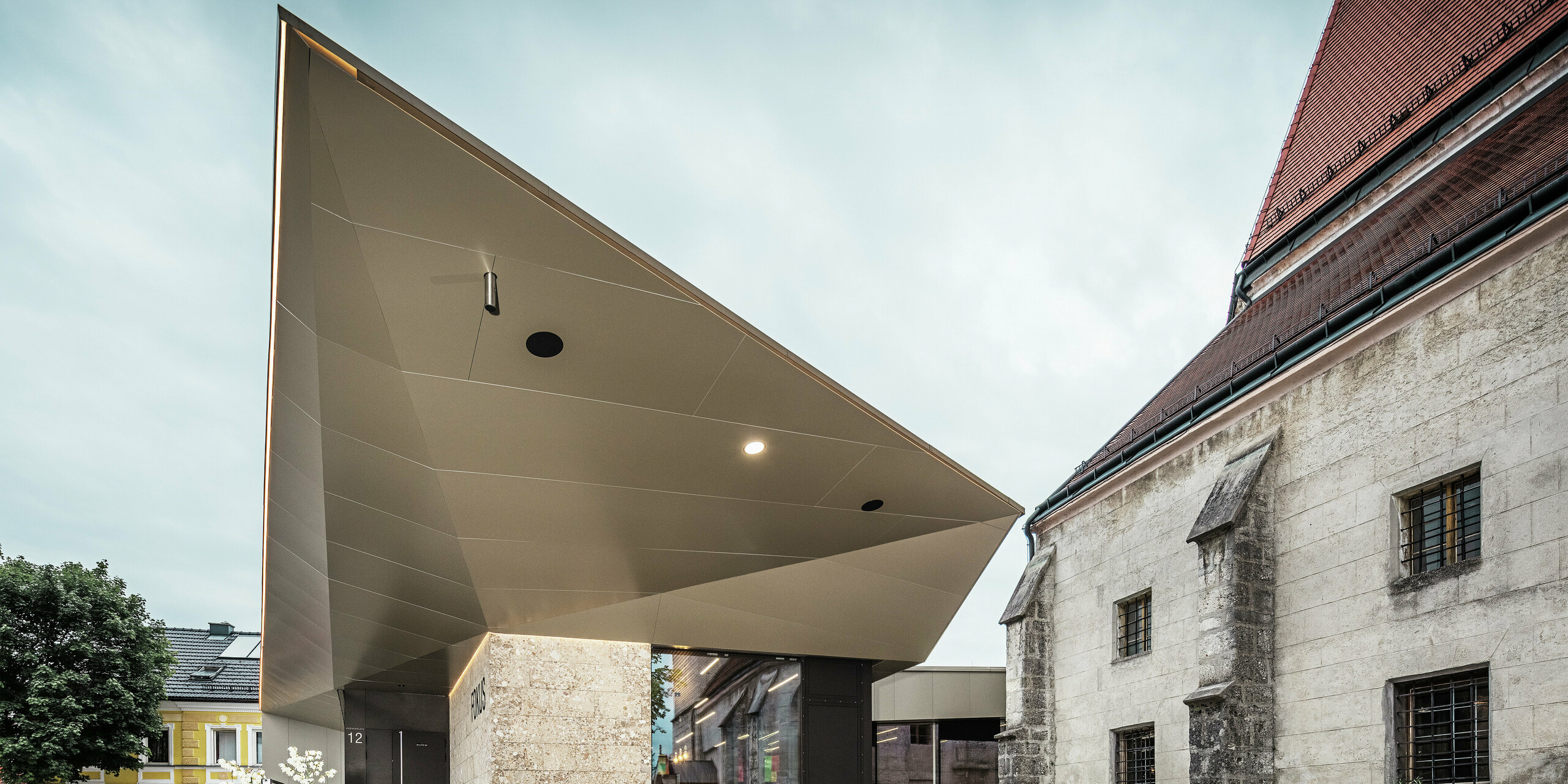 Ein Blick unter das kantig gefaltete Vordach offenbart die raffinierte Verarbeitung der bronzefarbenen PREFA Aluminium Verbundplatten. Diese bieten optimalen Korrosionsschutz, sind UV-beständig und verleihen der Konstruktion eine futuristische, fast schwerelose Ästhetik.