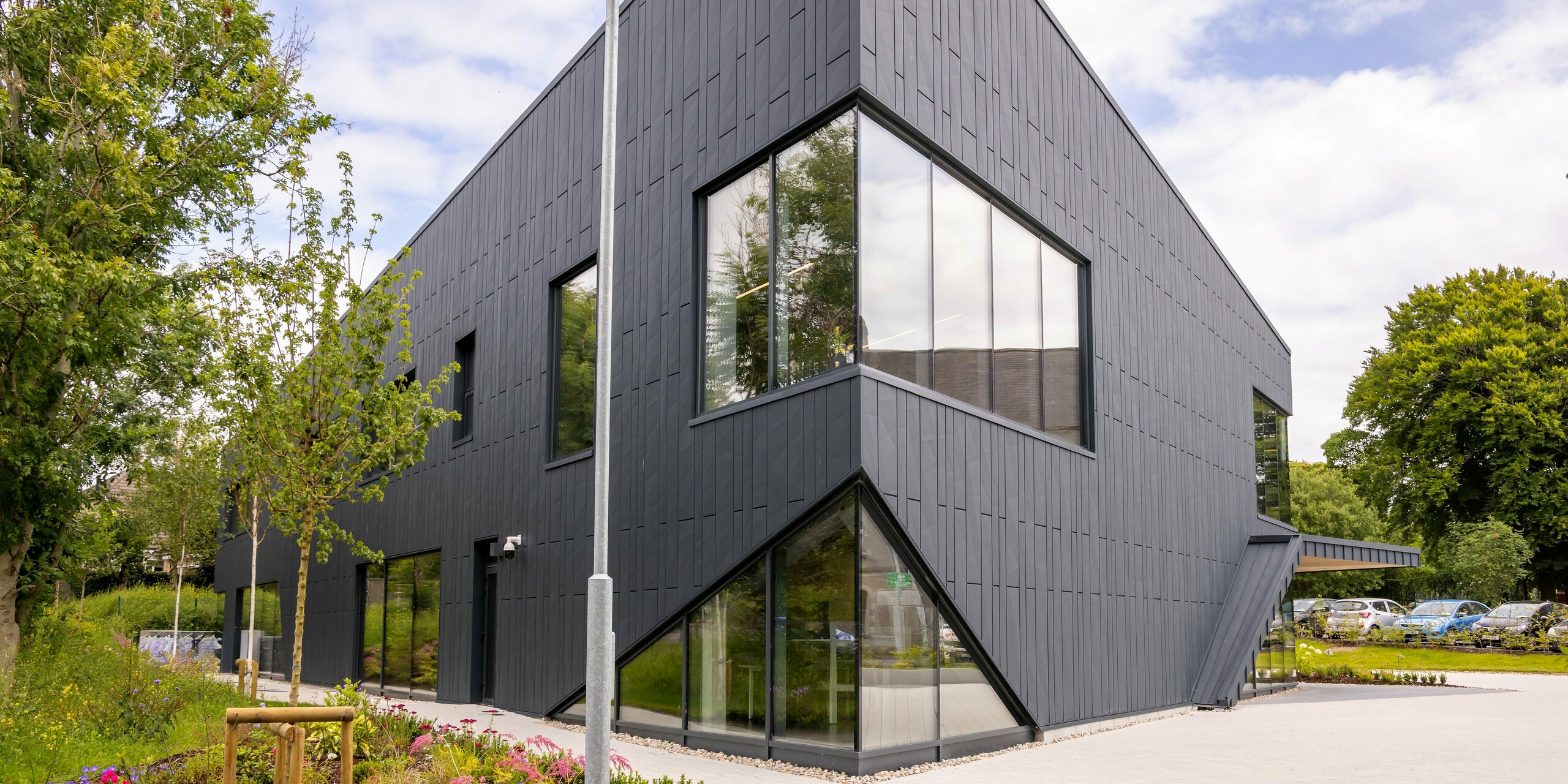 Front of the CREW building in Galway, Ireland, with PREFA Siding.X façade panels in the colour P.10 anthracite. The clean lines and large windows emphasise the contemporary architecture of the building. The façade made of robust and durable aluminium gives the building an elegant, modern look that is harmoniously complemented by the surrounding greenery.