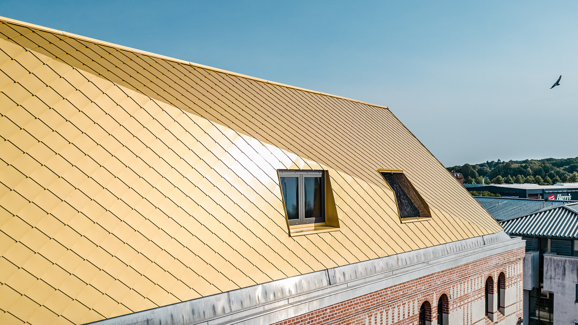 The roof with the Maya gold aluminium rhomboid tiles and a fold from up close, part of the listed façade can be seen.