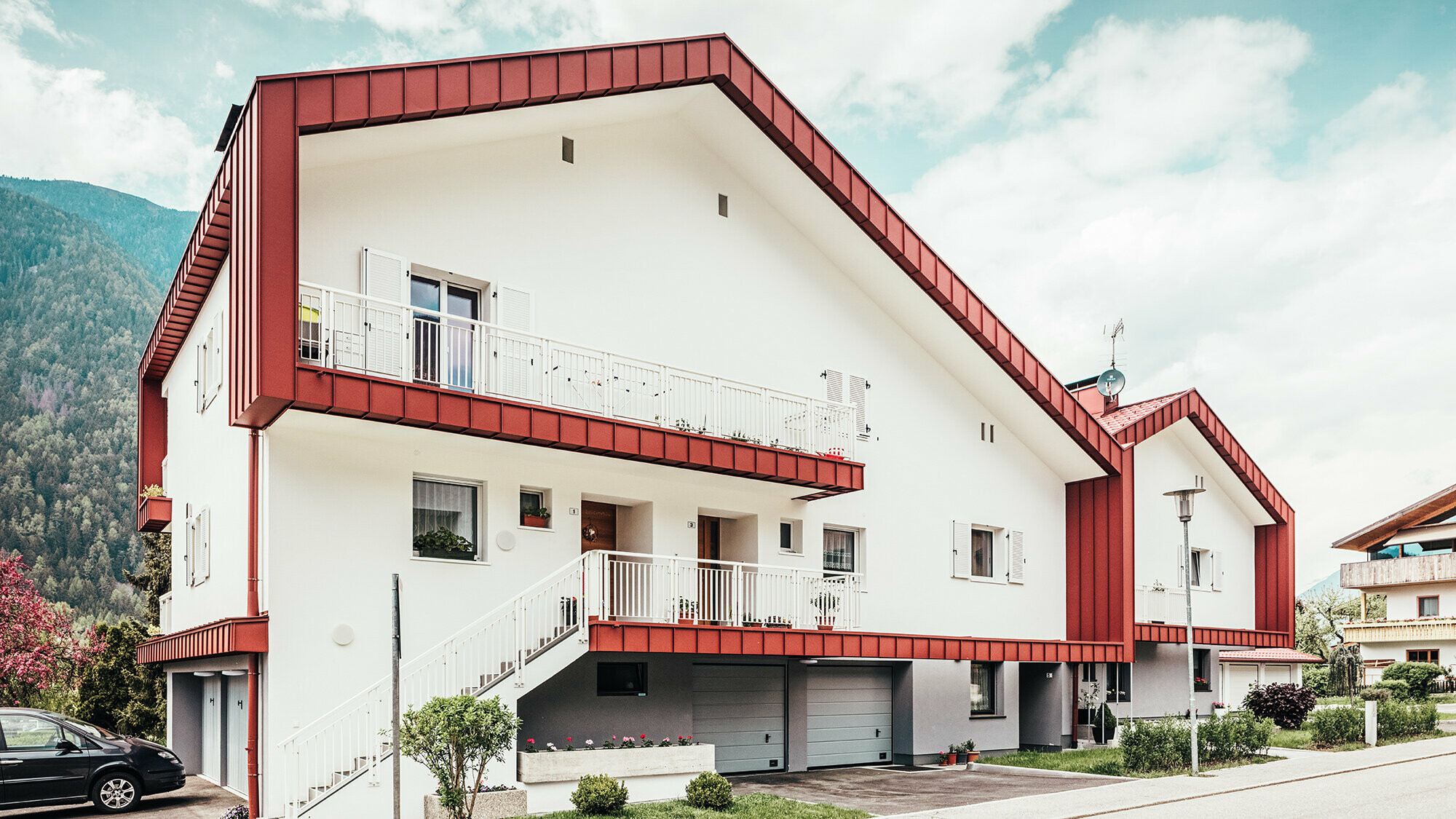 After photo of the residential building in Gais: the oxide red roof panel frames the two adjoining residential buildings.