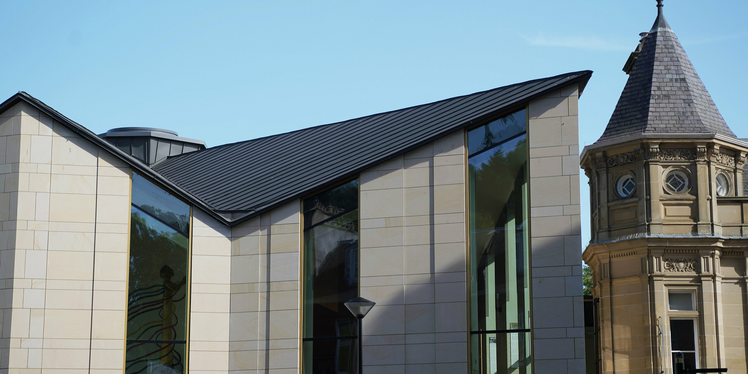 Side view of 'The Great Tapestry of Scotland' museum in Galashiels, which is characterised by a modern PREFALZ roof in P.10 zinc grey. The roof with its clear, geometric lines forms an attractive contrast to the traditional sandstone façades of the neighbouring buildings. The unique roof construction with its striking edges gives the building a contemporary flair and emphasises the combination of historical architecture and modern design.