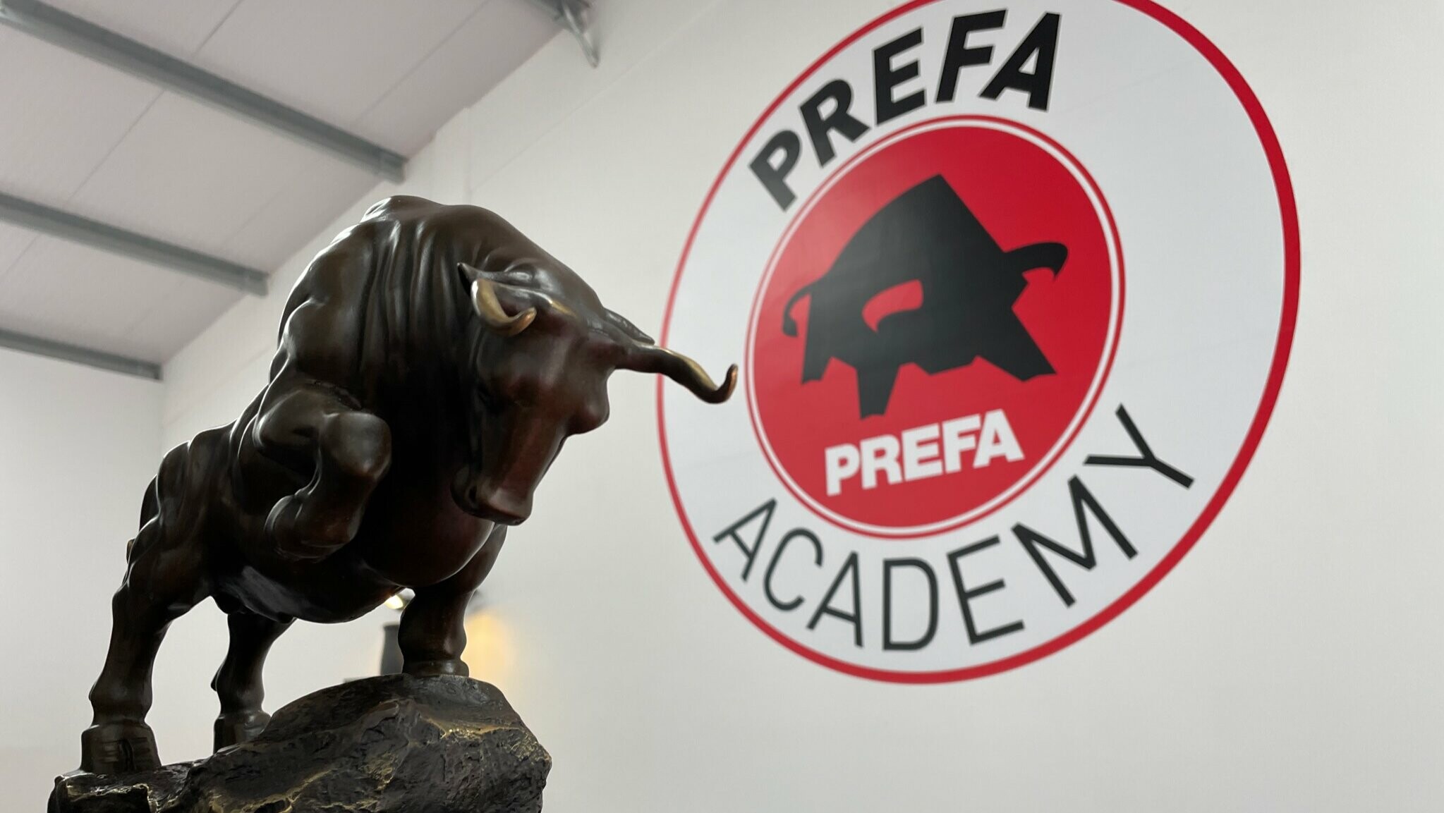 Photo of a bull as a statue. The logo of the PREFA Academy in the UK can be seen in the background.