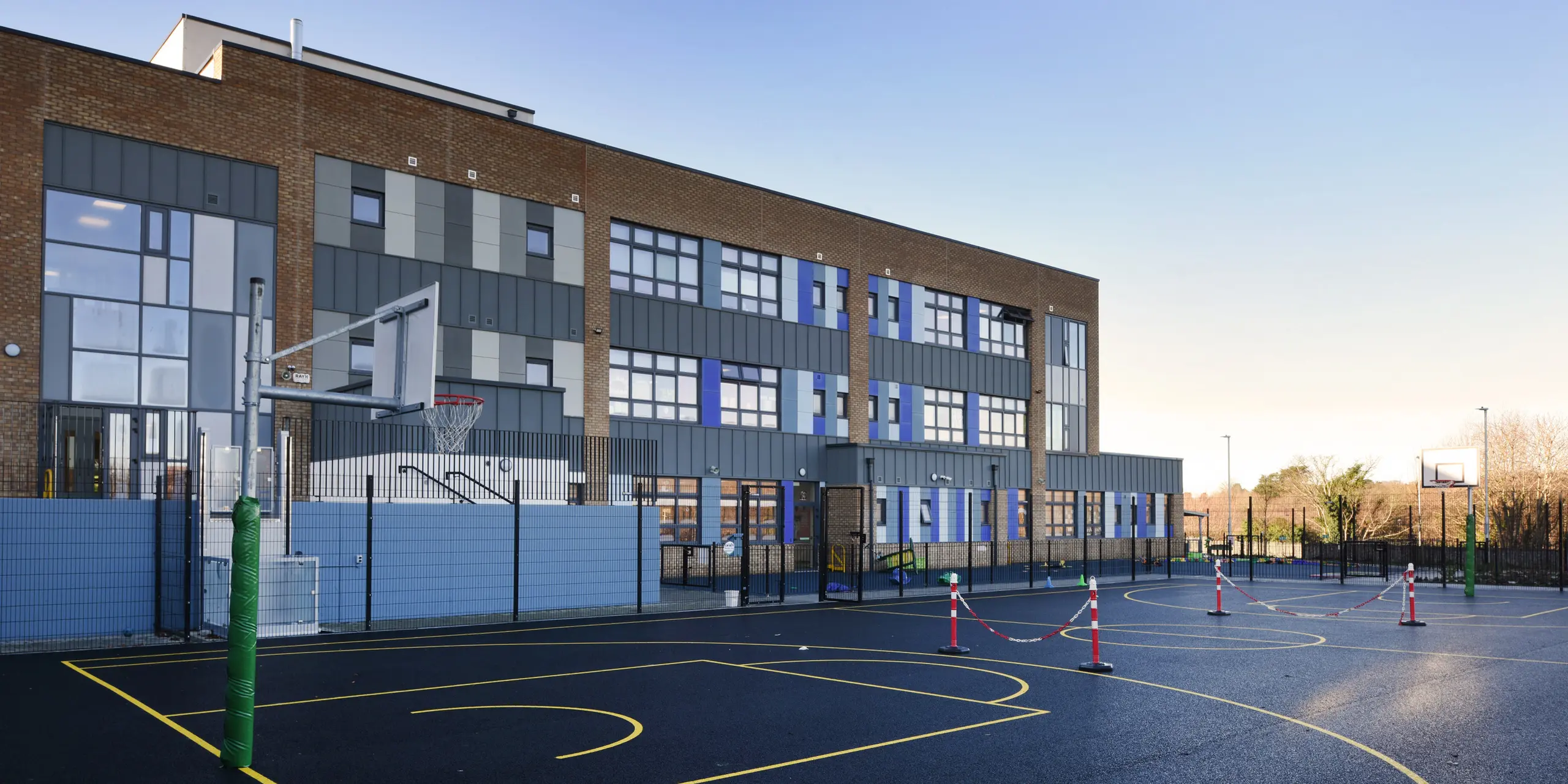 Rear of the Pelletstown Educate Together National School in Dublin, overlooking the basketball court. The light grey aluminium cladding made from PREFALZ standing seam P.10 light grey complements the school's brick façade and offers weather-resistant protection and a modern design.