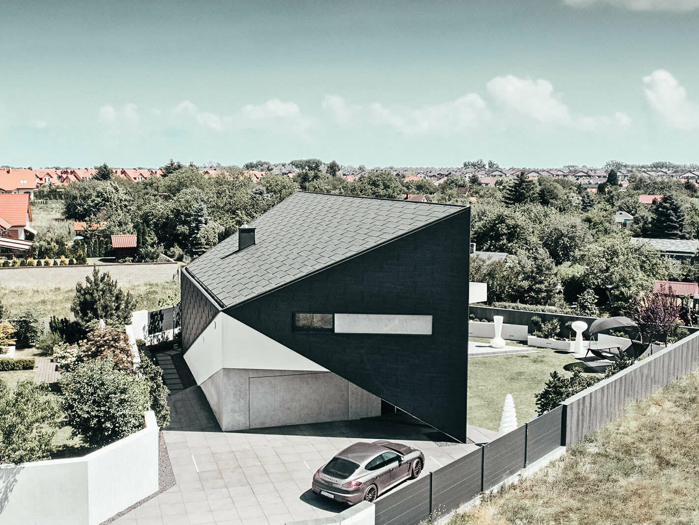 Bird's eye view of the house in triangular format. The beautiful façade covered in PREFA Siding.X in p.10 anthracite varies in appearance depending on the incidence of light. A car is parking in the driveway.
