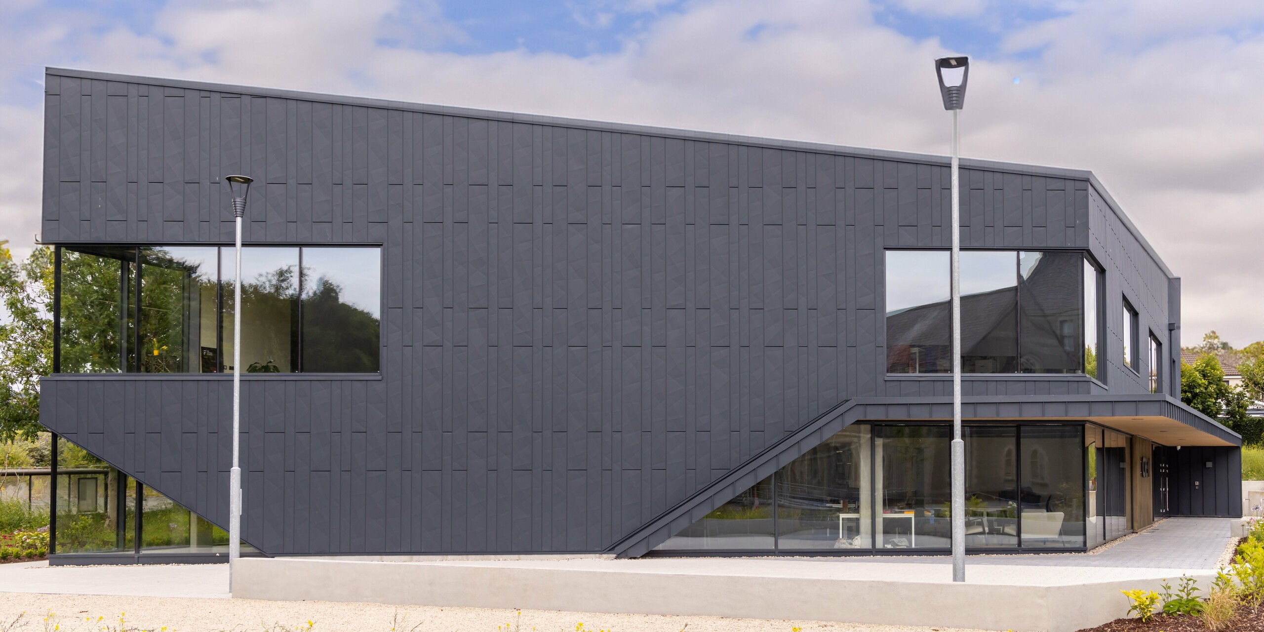 Side view of the CREW building in Galway, Ireland, with modern PREFA aluminium façade made of Siding.X façade panels and PREFALZ in P.10 anthracite. The geometric lines and large window areas emphasise the contemporary architecture. The high-quality sheet metal cladding gives the building an elegant and professional appearance, while the surrounding landscape rounds off the modern design.