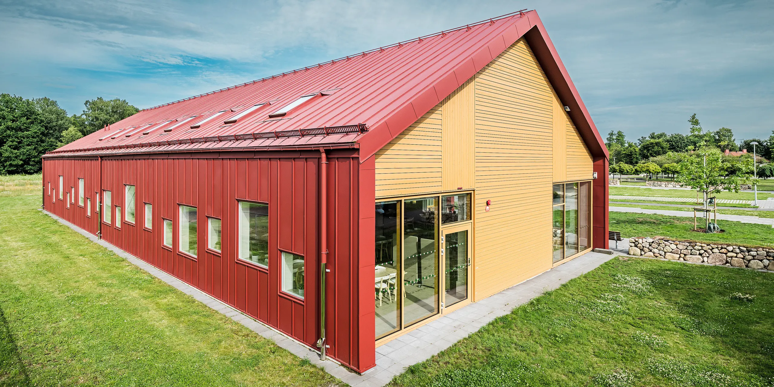 The gable end of the Gröna Hjärtat school canteen in Broby, Sweden, features an impressive combination of PREFALZ in oxide red, timber and generous glazed areas. The timber cladding on the gable end provides an attractive contrast to the durable aluminium cladding on the rest of the building. Numerous windows and roof windows allow plenty of natural light into the building, whilst the contemporary design emphasises the architectural quality and energy efficiency of the structure. The building is an outstanding example of contemporary architecture featuring materials with sustainability and innovative design.