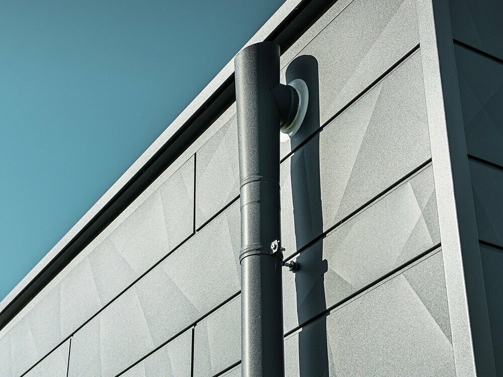 PREFA downpipe with PREFA parapet outlet connector in P.10 anthracite on a PREFA Siding.X facade, in P.10 anthracite as well
