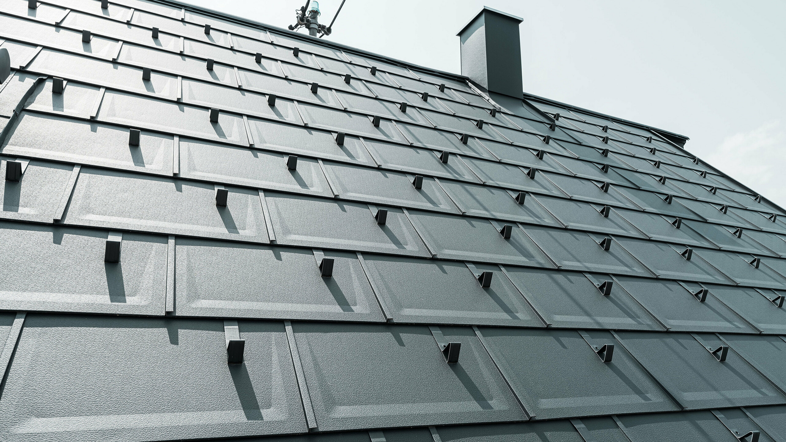 Detailed view of the PREFA R.16 roof tile in colour P.10 anthracite. PREFA snow guards and a smoke hood can be seen on the roof.