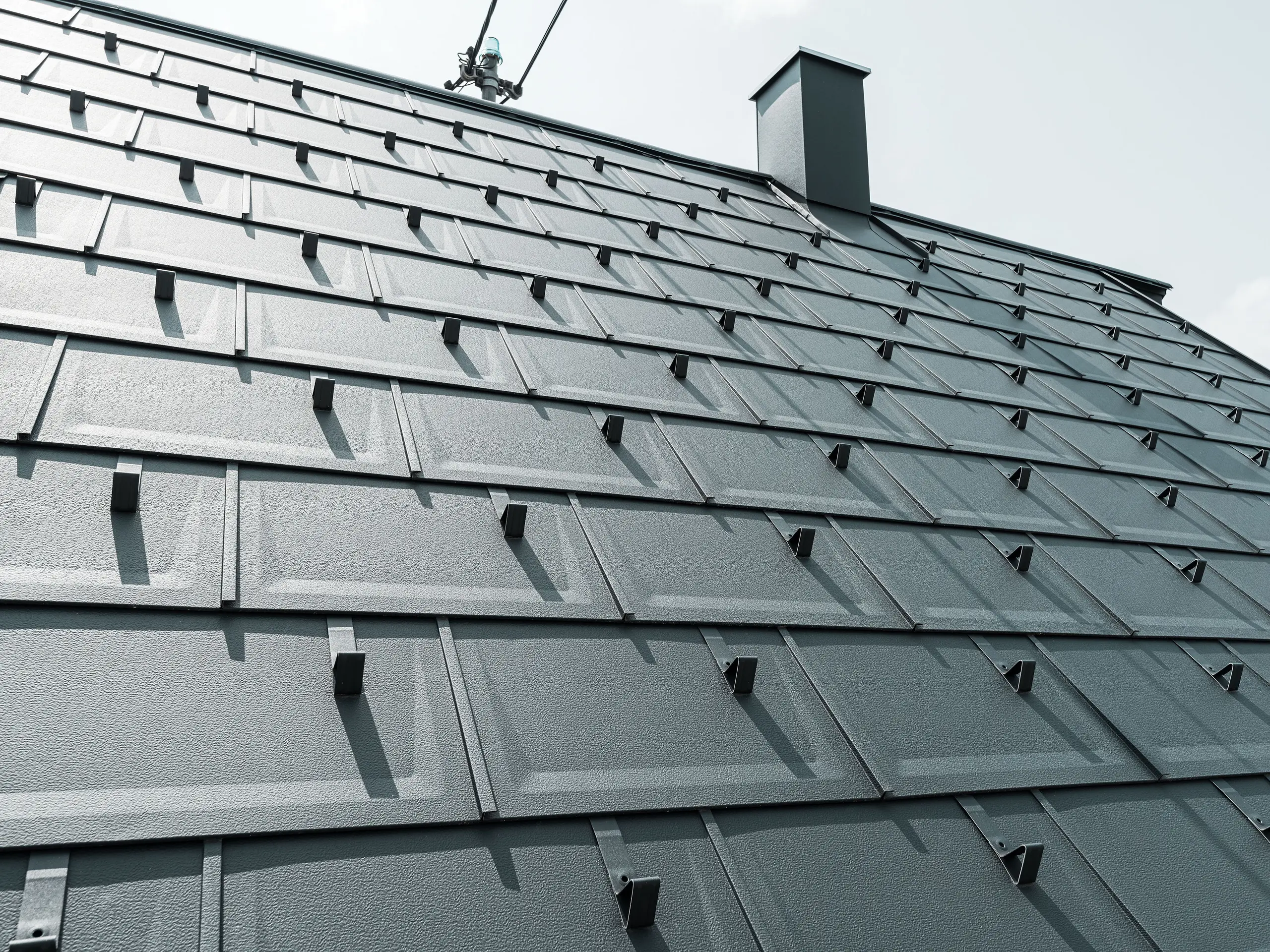 Detailed view of the PREFA R.16 roof tile in colour P.10 anthracite. PREFA snow guards and a smoke hood can be seen on the roof.