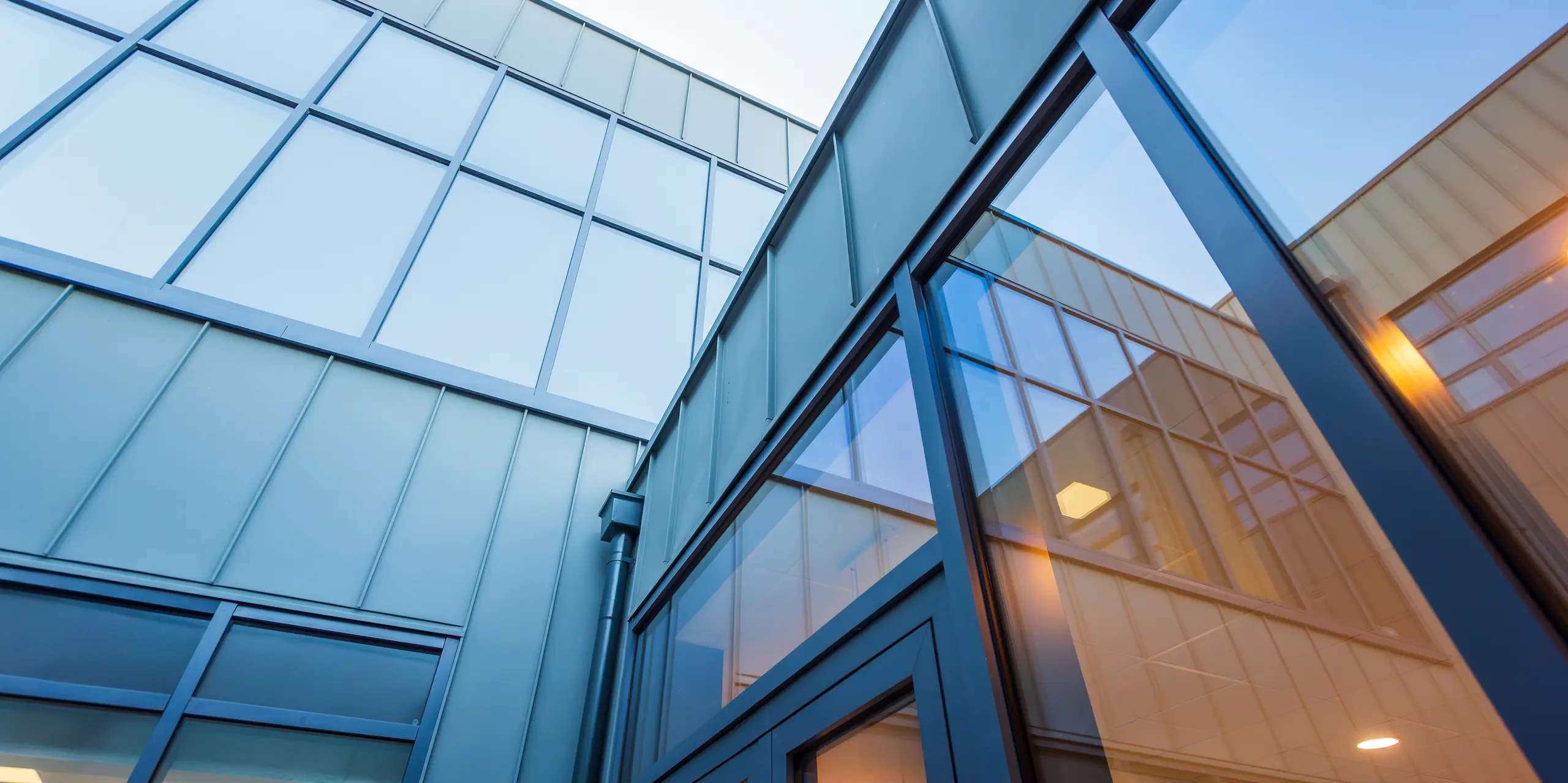 A worm's eye view of the modern PREFALZ standing seam aluminium facade in P.10 light grey of Scoil Mhuire Naofa in Carrigtwohill, Republic of Ireland. Large window areas and precise standing seam tracks emphasise the contemporary architecture and ensure a light-flooded, elegant design.