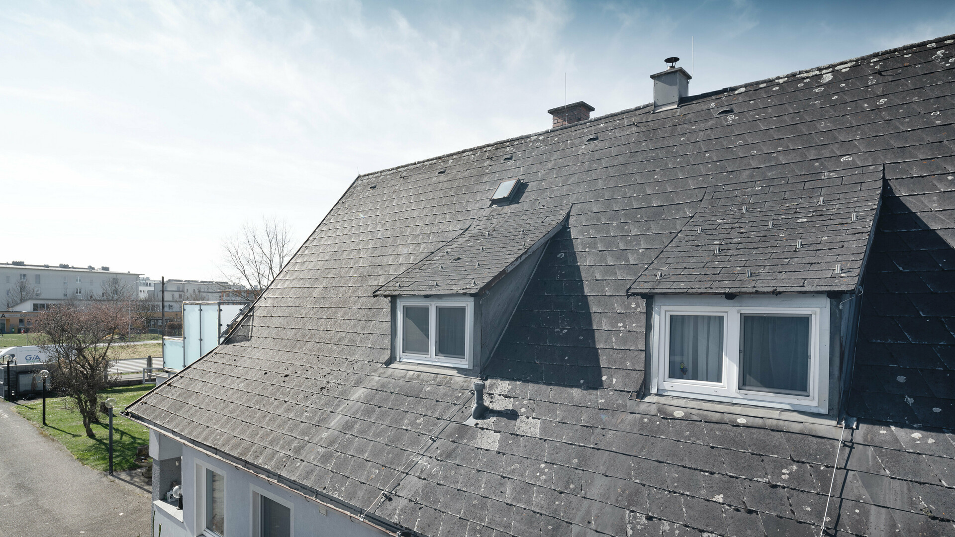 Close-up of an old Eternit roof showing signs of wear and lichen growth. The roof has two dormers, which are visible. Photograph taken before the roof renovation.