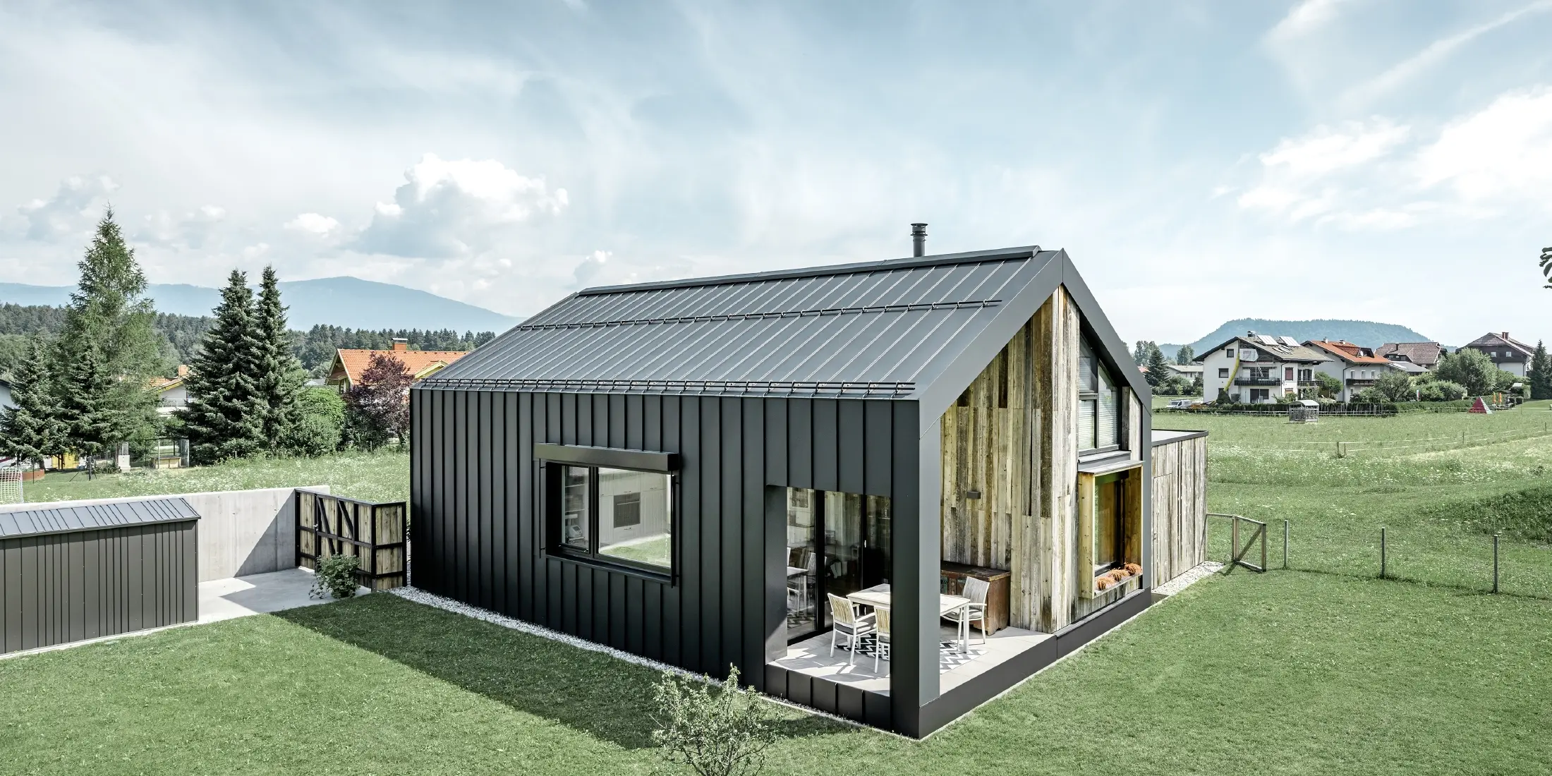 Detached house with gable roof, roof and façade are covered with PREFALZ standing seam from PREFA in P.10 anthracite. The panels of the roof surface extend across the façade. Part of the façade is clad with weathered wood.