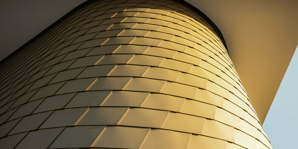 Detailed view of a curved wall cladding with the PREFA façade shingle in maya gold