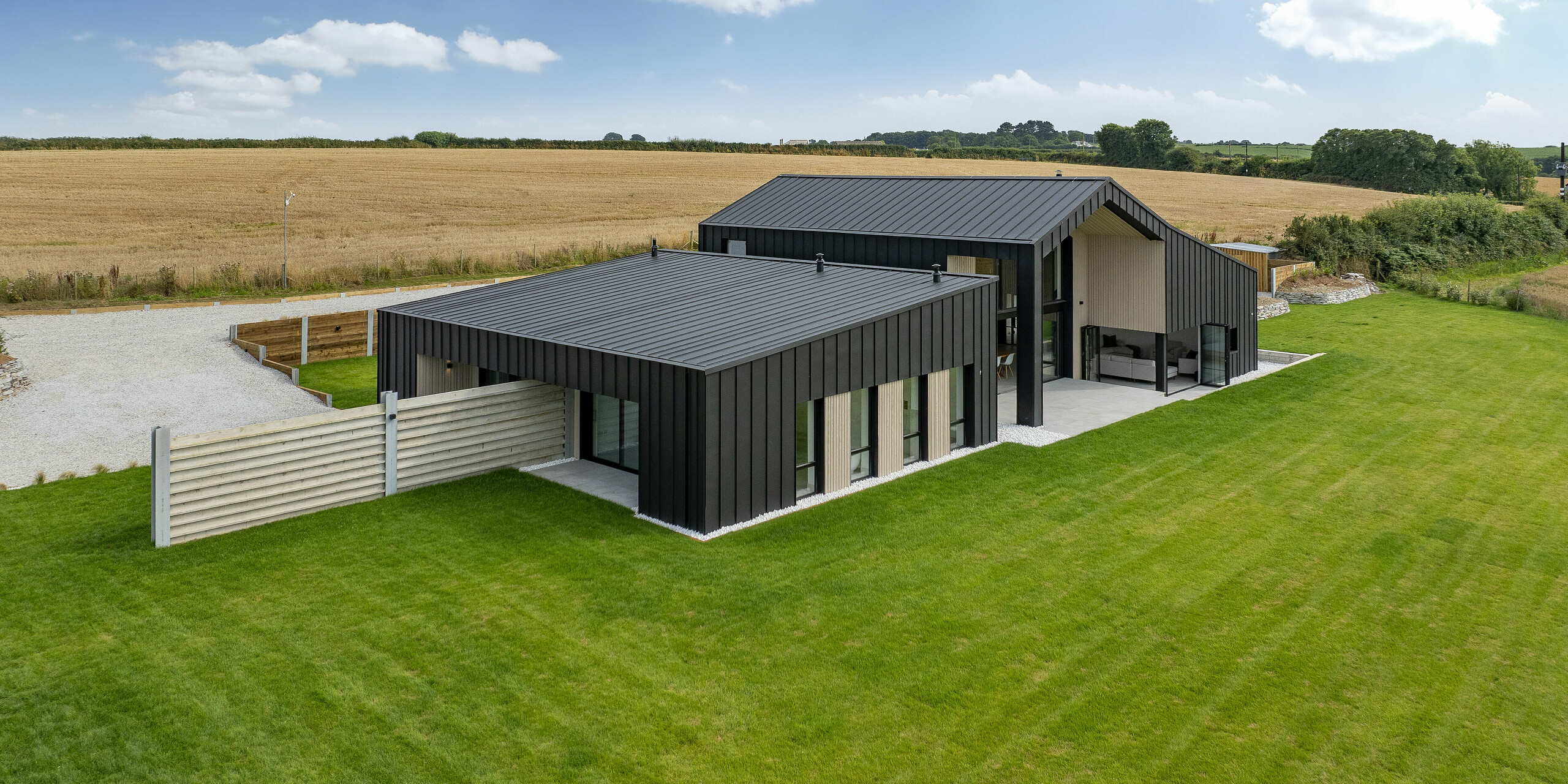 Wide-angle view of the back of ‘The Hide’ in Cornwall. The modern detached house with PREFALZ aluminium roof and facade cladding blends harmoniously into the rural surroundings with its many fields. The anthracite-coloured standing seam roofing emphasises the minimalist design while providing optimal weather protection.