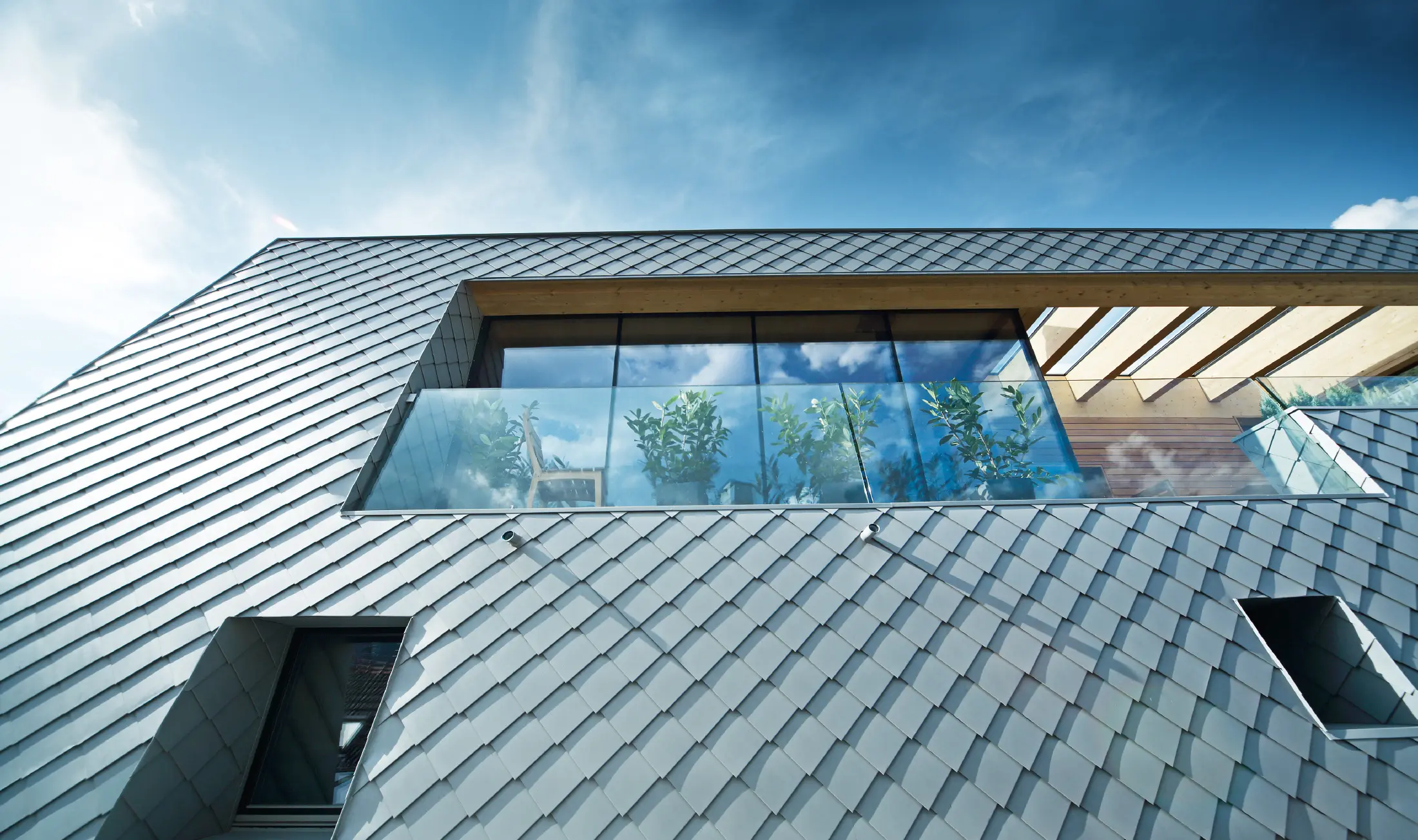 Modern ausgebautes Dachgeschoss mit großflächiger Dachterrasse, bodentiefen Glasfronten und patinagrauer Dachdeckung in Rautenoptik, die fließend in die Fassade übergeht und zeitgemäße Architektur betont.