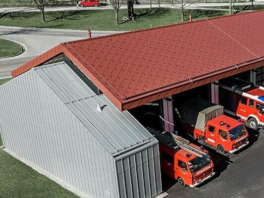 Fire station at the PREFA headquarters in Marktl, Austria, with a roof covered in red rhomboid roof tiles, and a standing seam roof and façade in metallic silver. Find more information about fire ratings here.