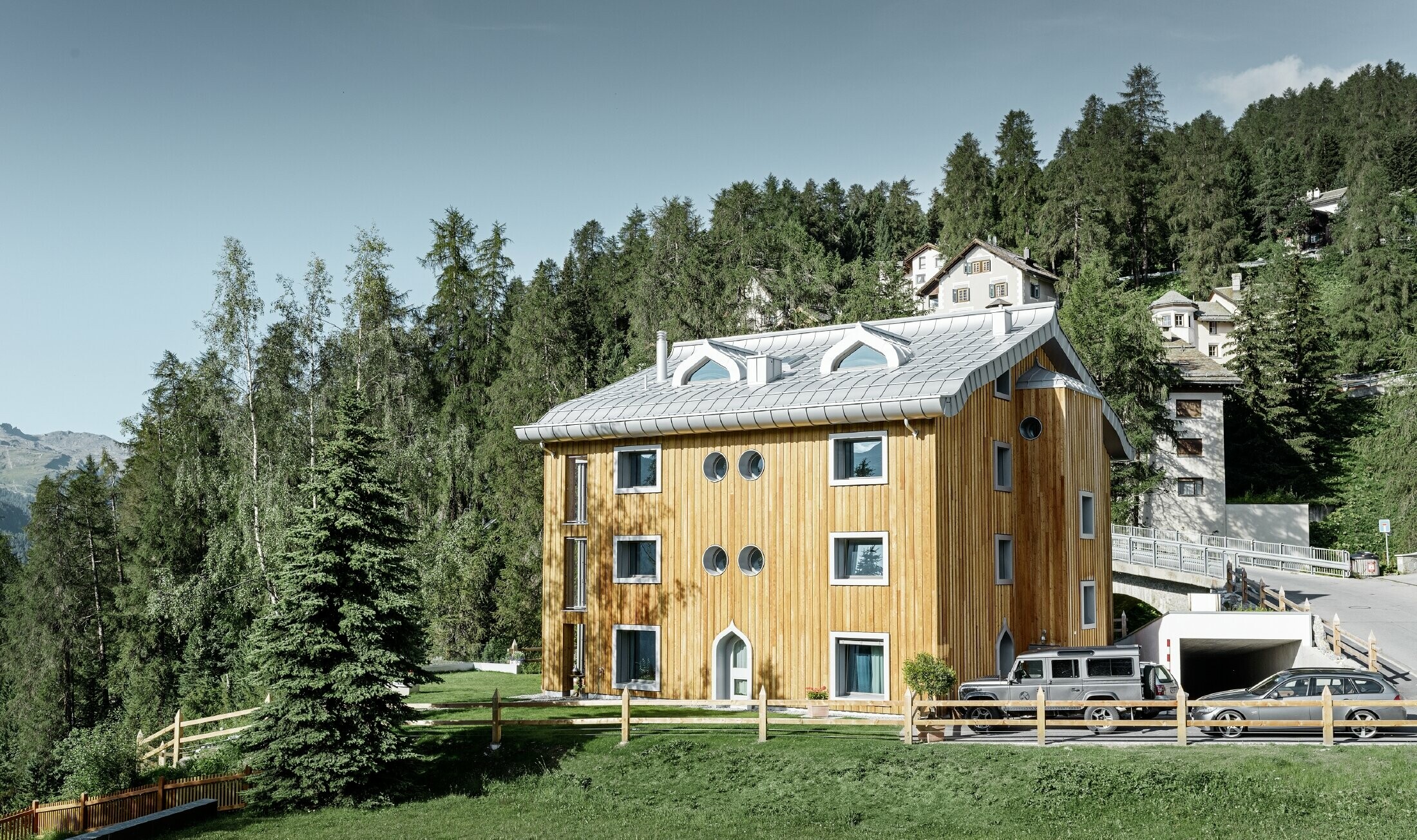 Residential complex in St. Moritz (Switzerland) with a wooden façade and an aluminium roof with undulating eaves in metallic silver