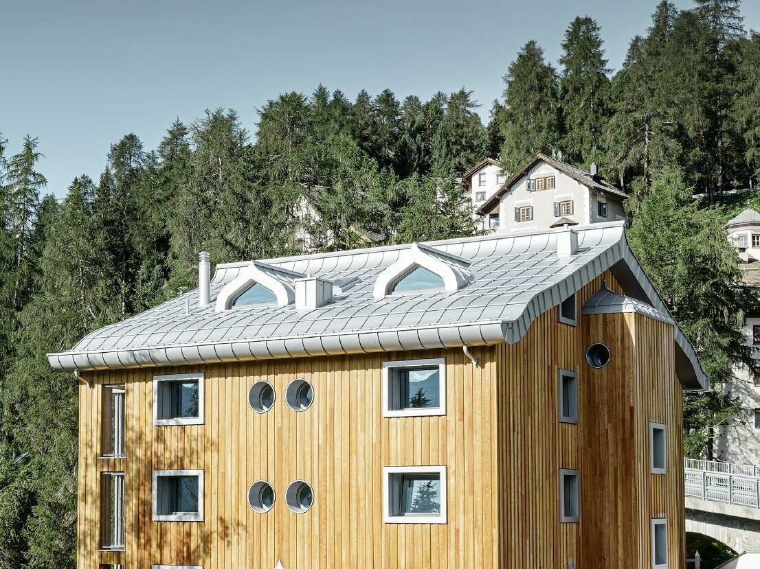 Residential complex in St. Moritz (Switzerland) with a wooden façade and an aluminium roof with undulating eaves in metallic silver