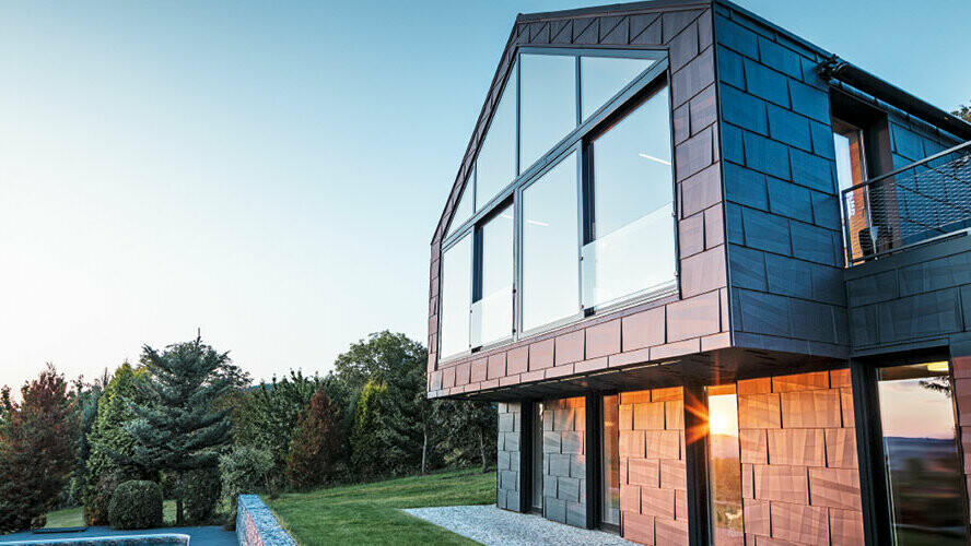 Modern detached house without eaves; with large windows and FX.12 façade in anthracite, photographed at sunset.
