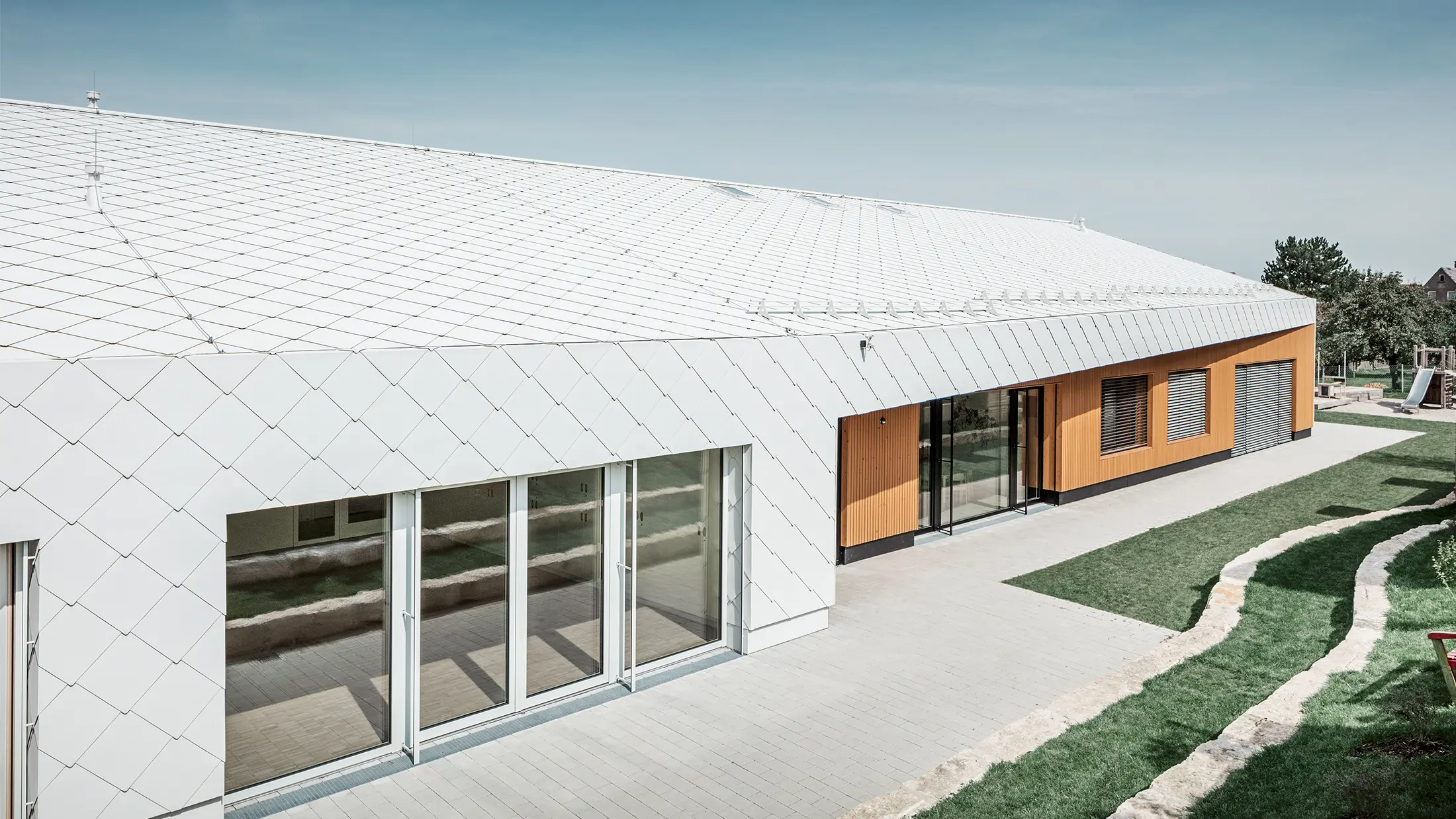 Nursery with the PREFA roof and façade tiles 44 in Prefa white, the roof surface extends over the façade; large window areas