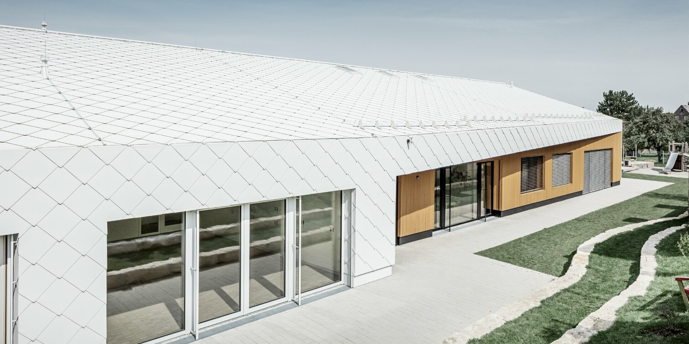 Nursery with the PREFA roof and façade tiles 44 in Prefa white, the roof surface extends over the façade; large window areas