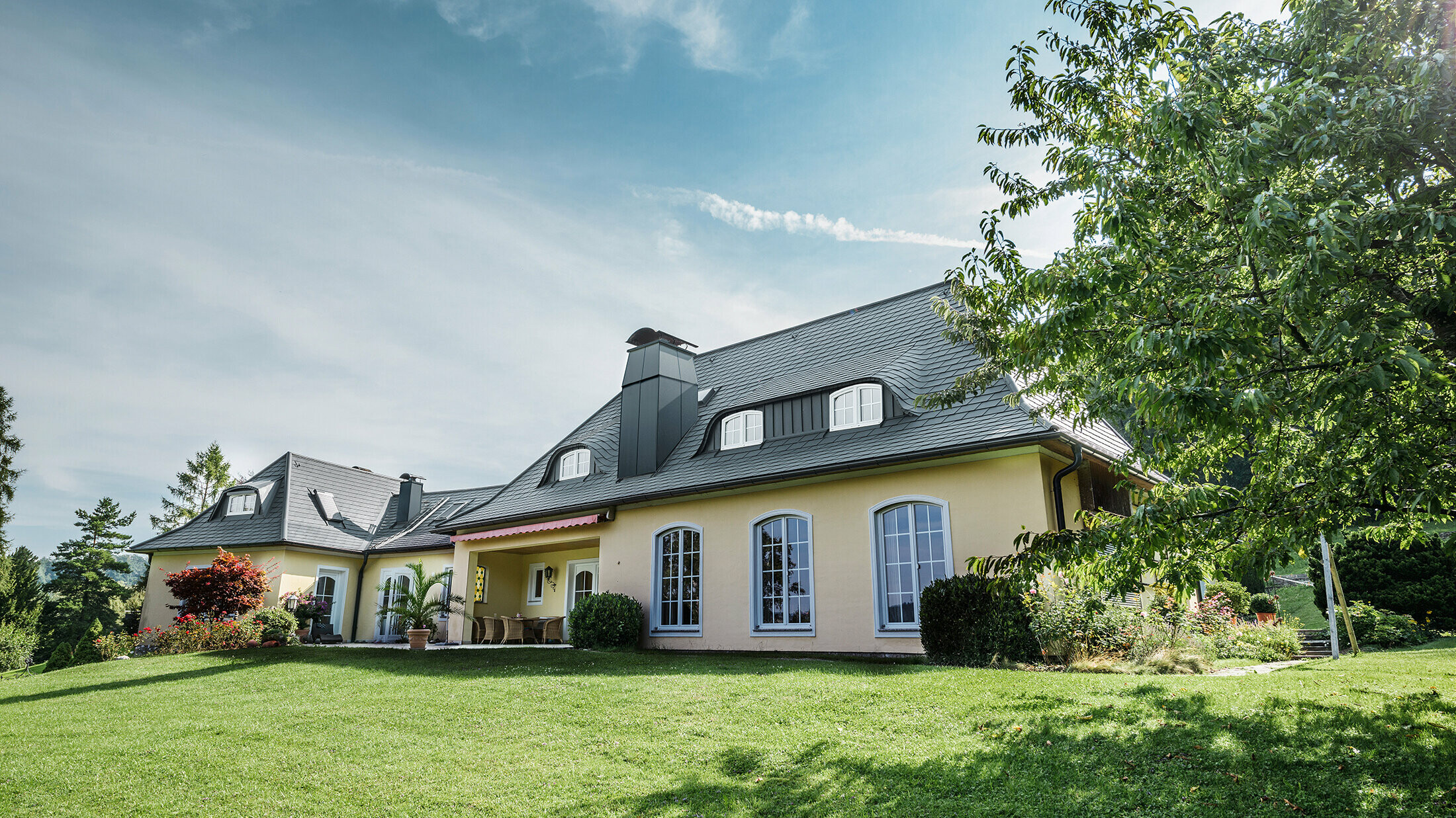 Classic detached house with curved dormers, roofed with the storm-proof PREFA roof shingle, with a 40-year material guarantee.