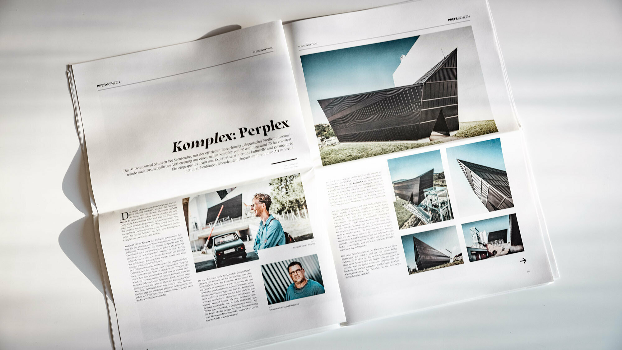 Frontal view of a tilted double page showing text as well as architecture photos and portraits of architects.
