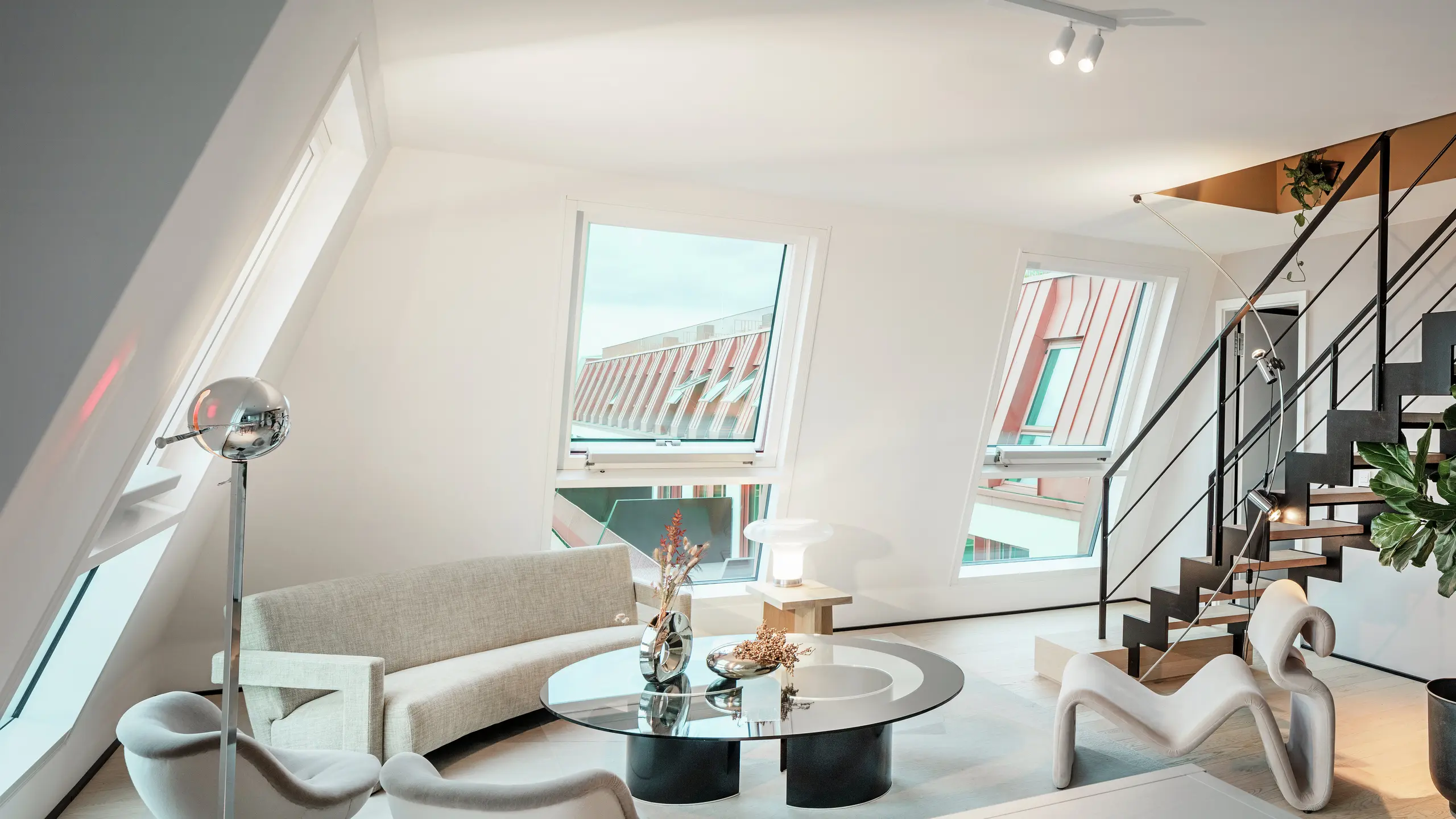 Internal view of a light-flooded penthouse in the Van B residential project in Munich with a view of the high-quality PREFALZ aluminium roof in the special colour IGP Orange HDP. The large windows allow plenty of daylight to enter and emphasise the modern living concept. Clear lines, designer furniture and the precise workmanship of the roof connections show how high-quality and stylish architecture can be implemented not only on the outside, but also on the inside.